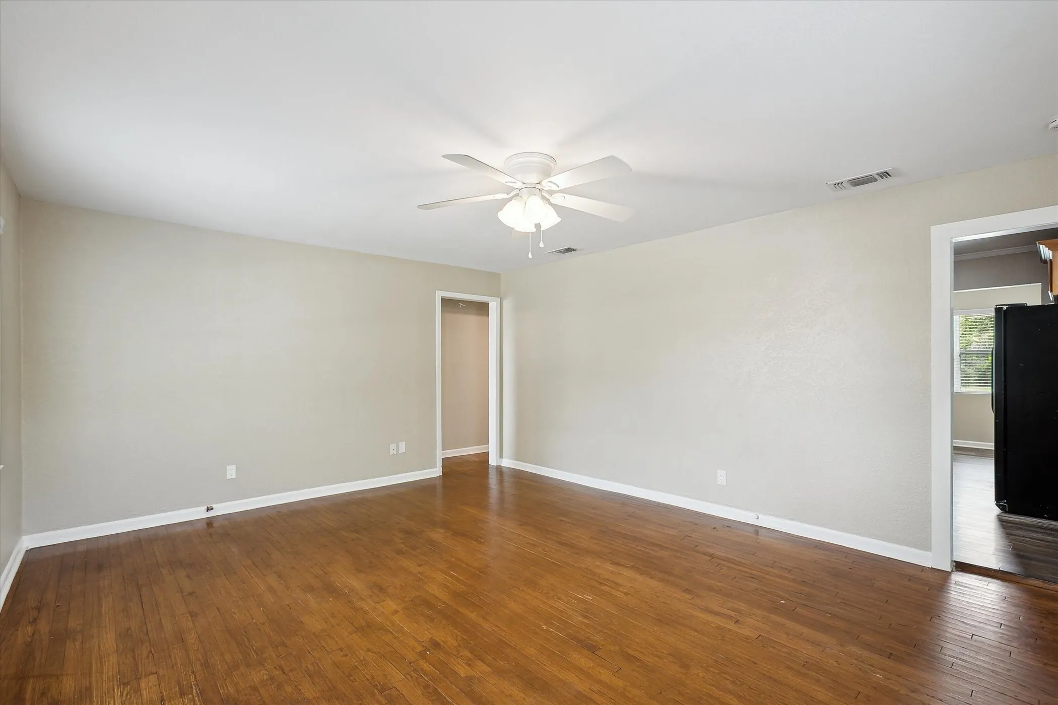 Spacious living room with beautiful wood floors throughout, neutral wall tones, and a ceiling fan with integrated lighting