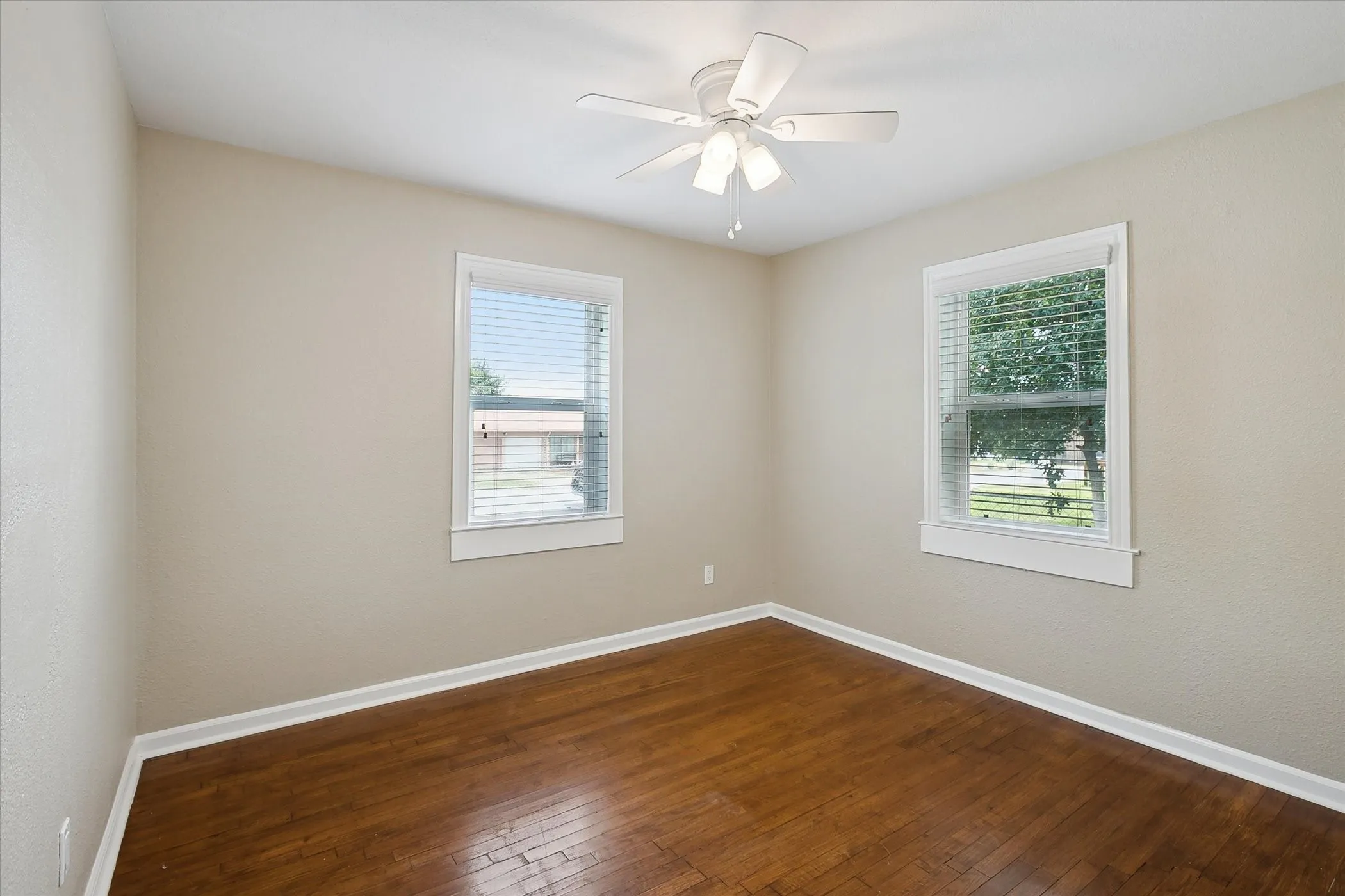 Hardwood flooring, painted walls, two windows with blinds, and a ceiling fan