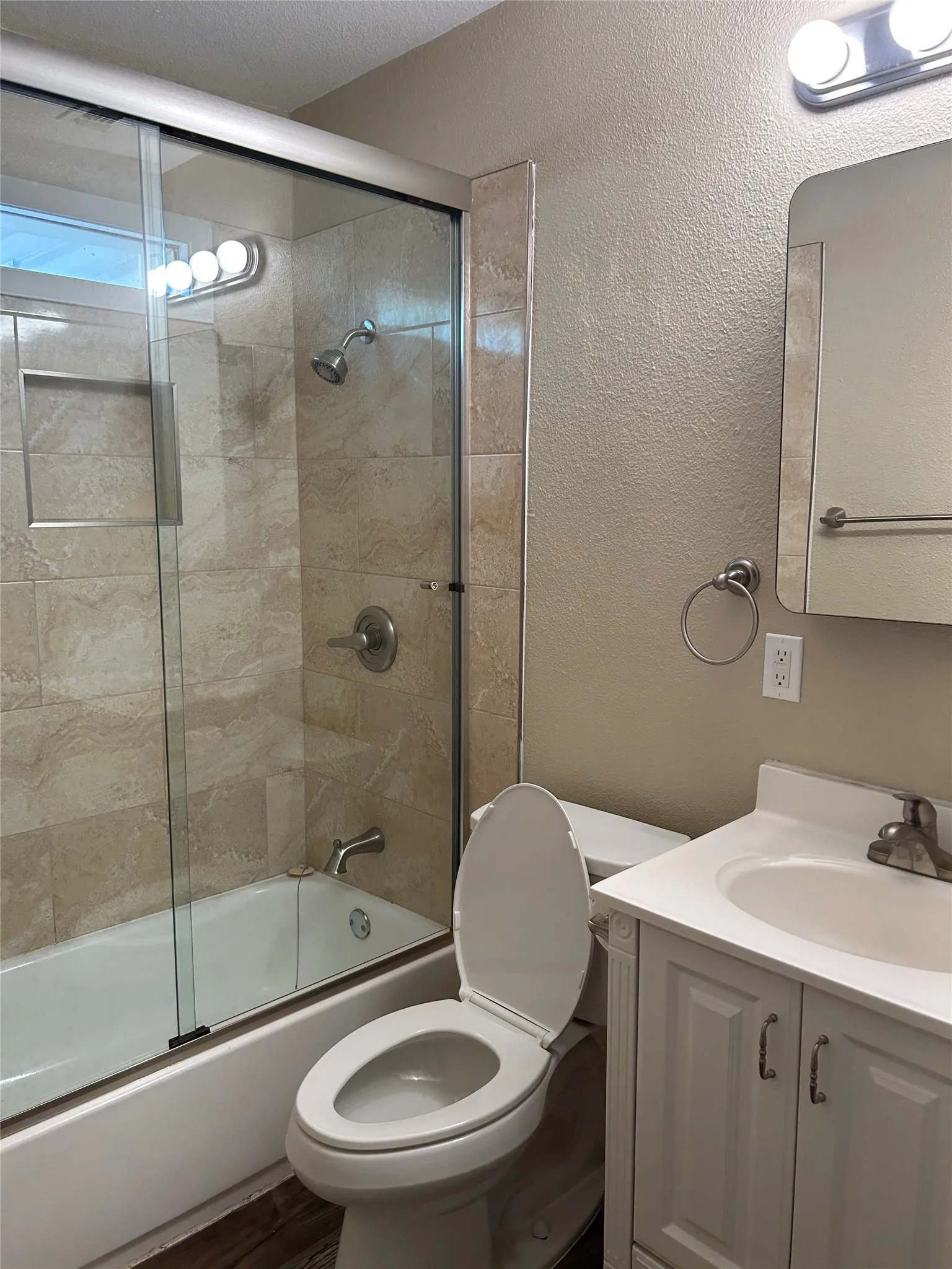 Bathtub with glass enclosure, tiled shower surround, wall-mounted showerhead, and built-in shower niche
