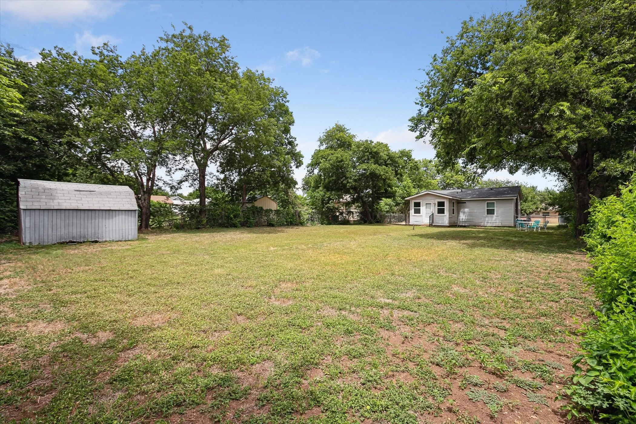 Expansive lot featuring a detached storage shed, mature trees, and a single-story dwelling with a light-colored exterior