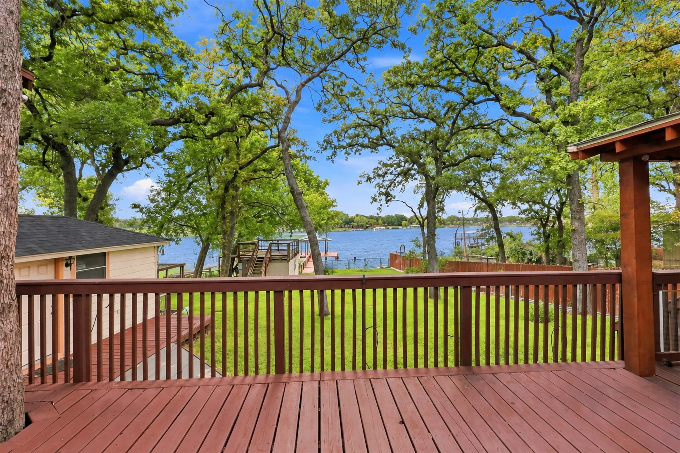 Expansive wood-finish deck with railing, surrounded by mature trees, overlooking a body of water