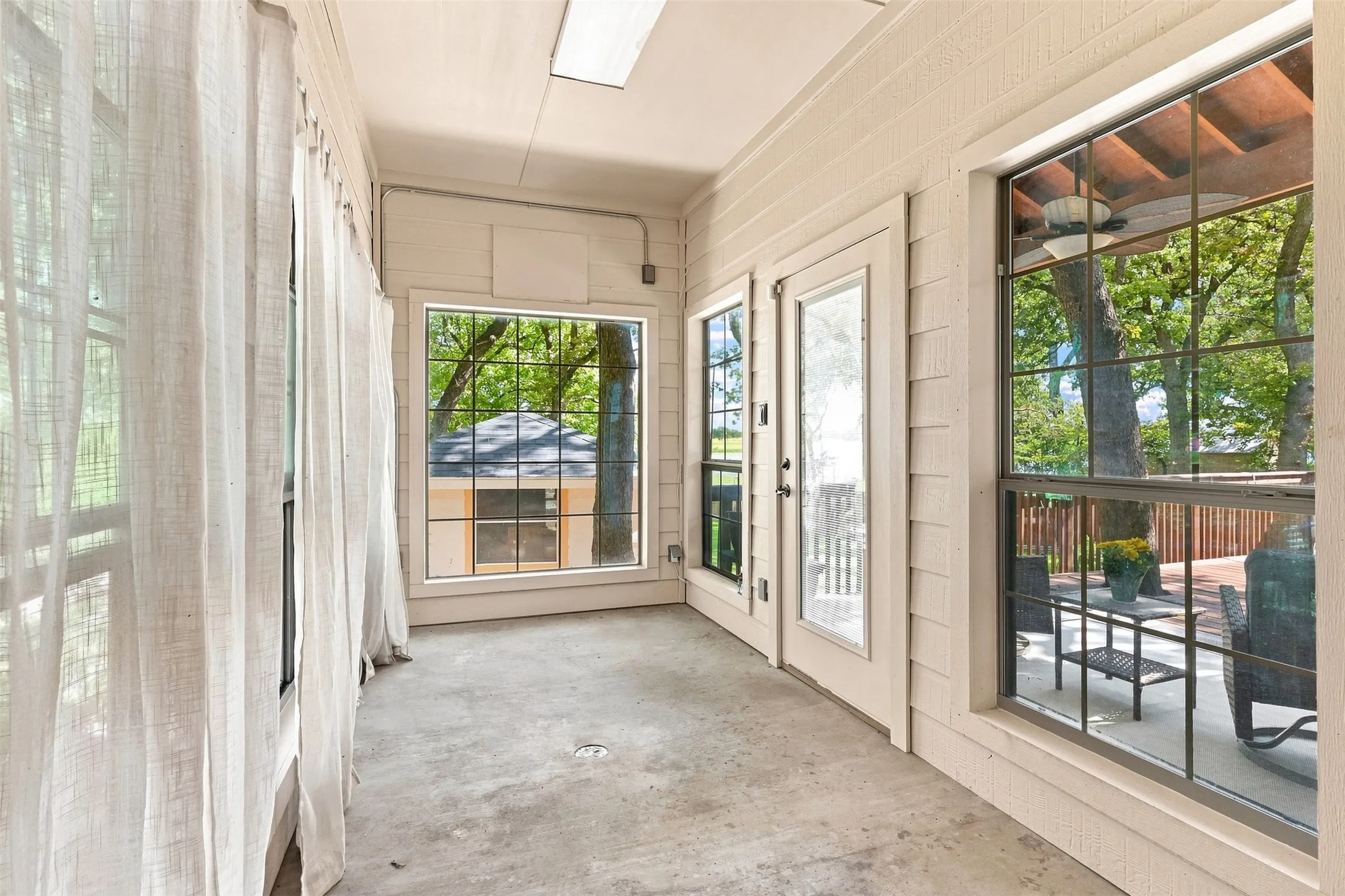 Enclosed porch featuring concrete flooring, multiple windows with grid patterns, and an exterior door with a glass panel