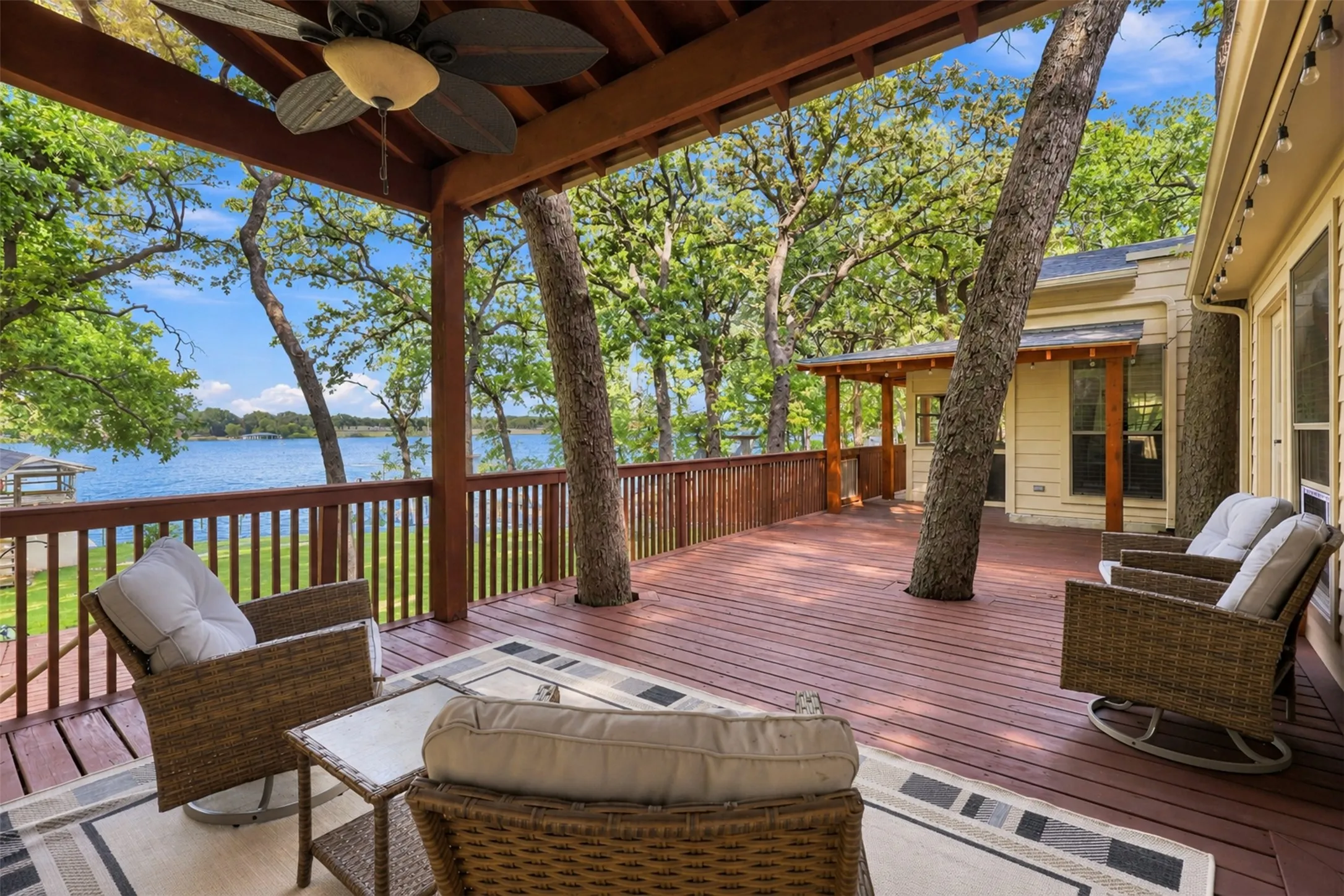 Expansive wood deck with a built-in ceiling fan, wood railing, and mature trees integrated into the design