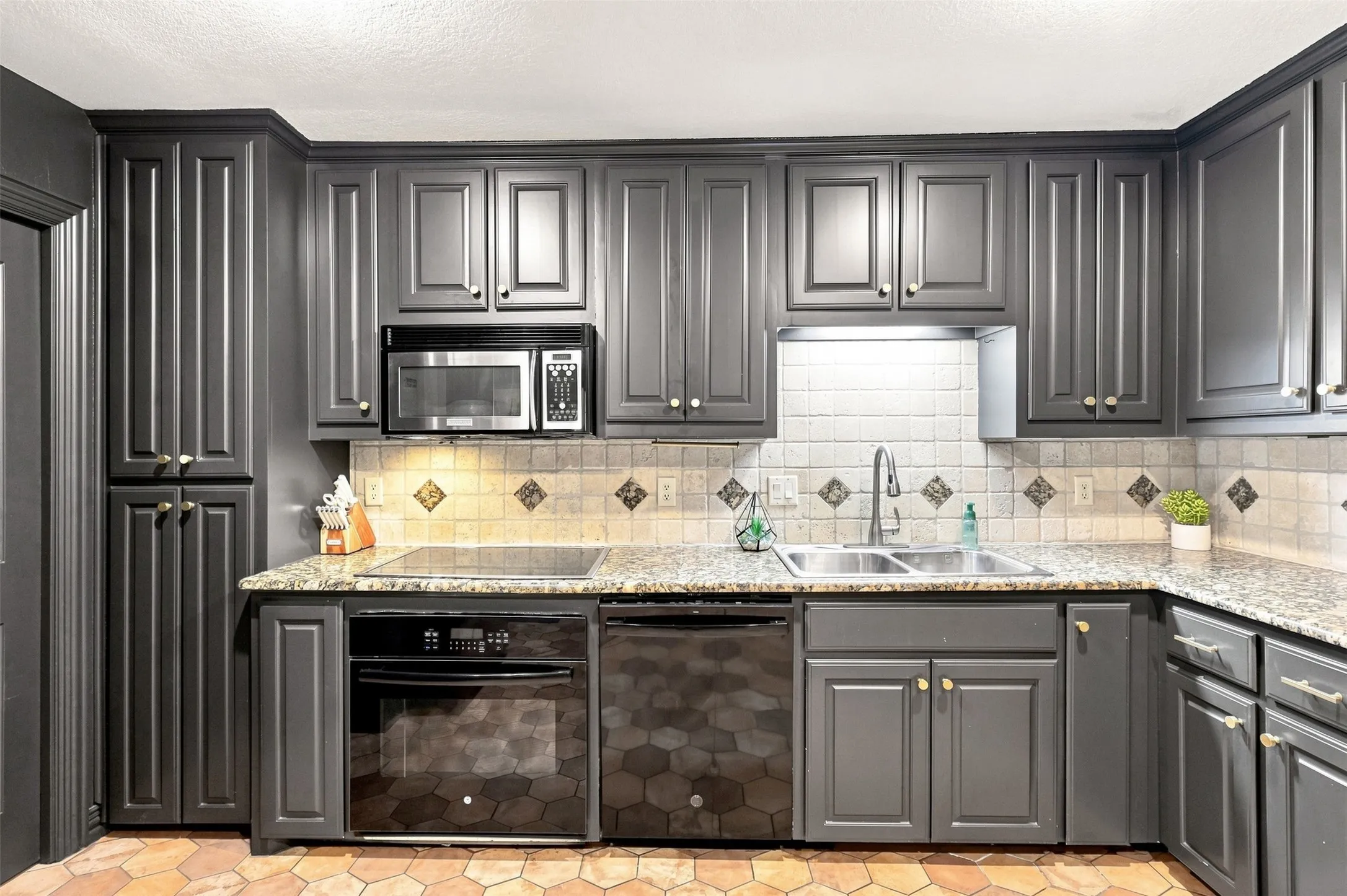 Kitchen featuring dark cabinetry, speckled countertops, a tile backsplash with diamond accents, and stainless steel appliances
