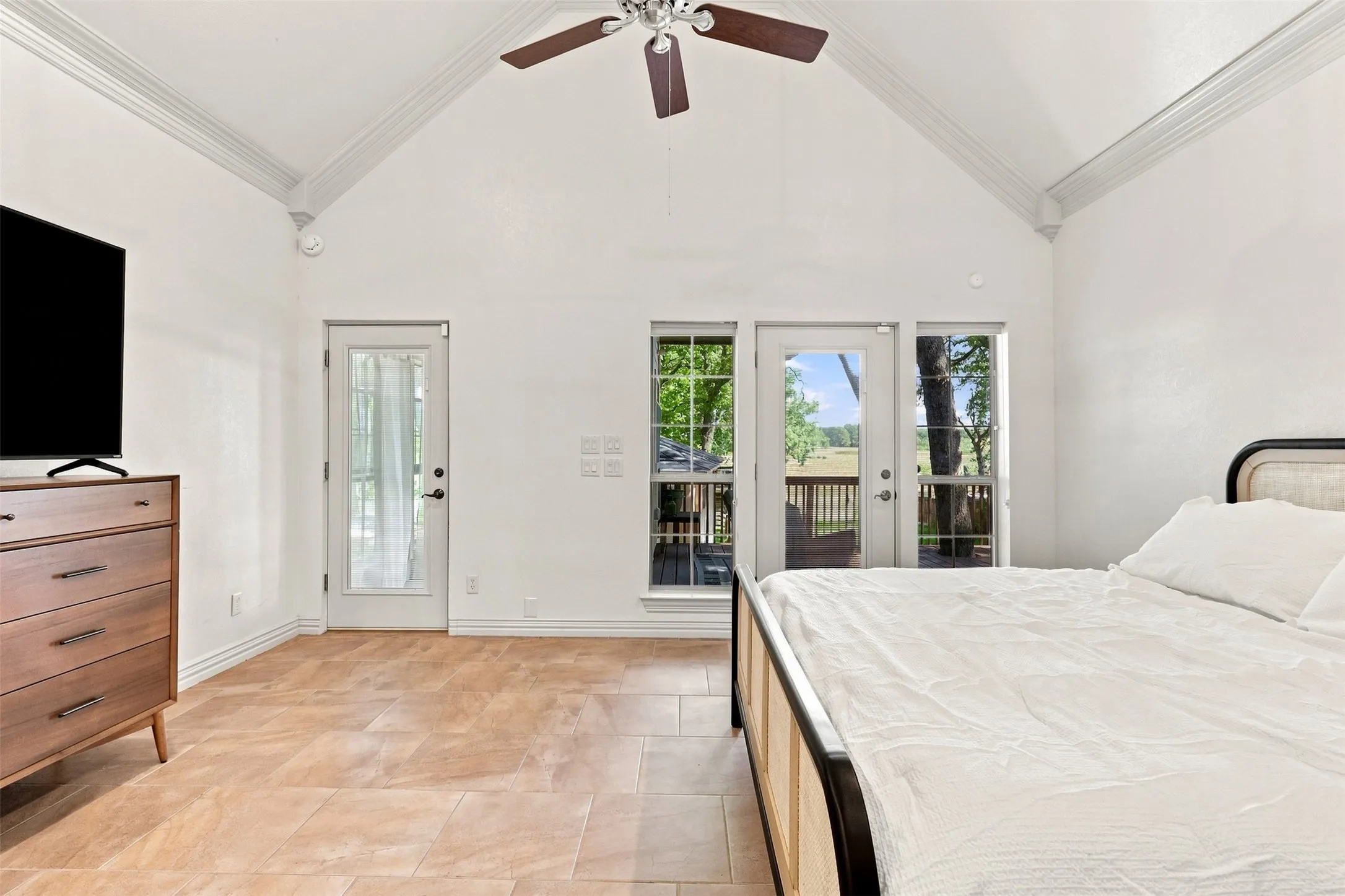 Vaulted ceiling with crown molding, ceiling fan, tile flooring, and glass-paned doors leading to an exterior deck