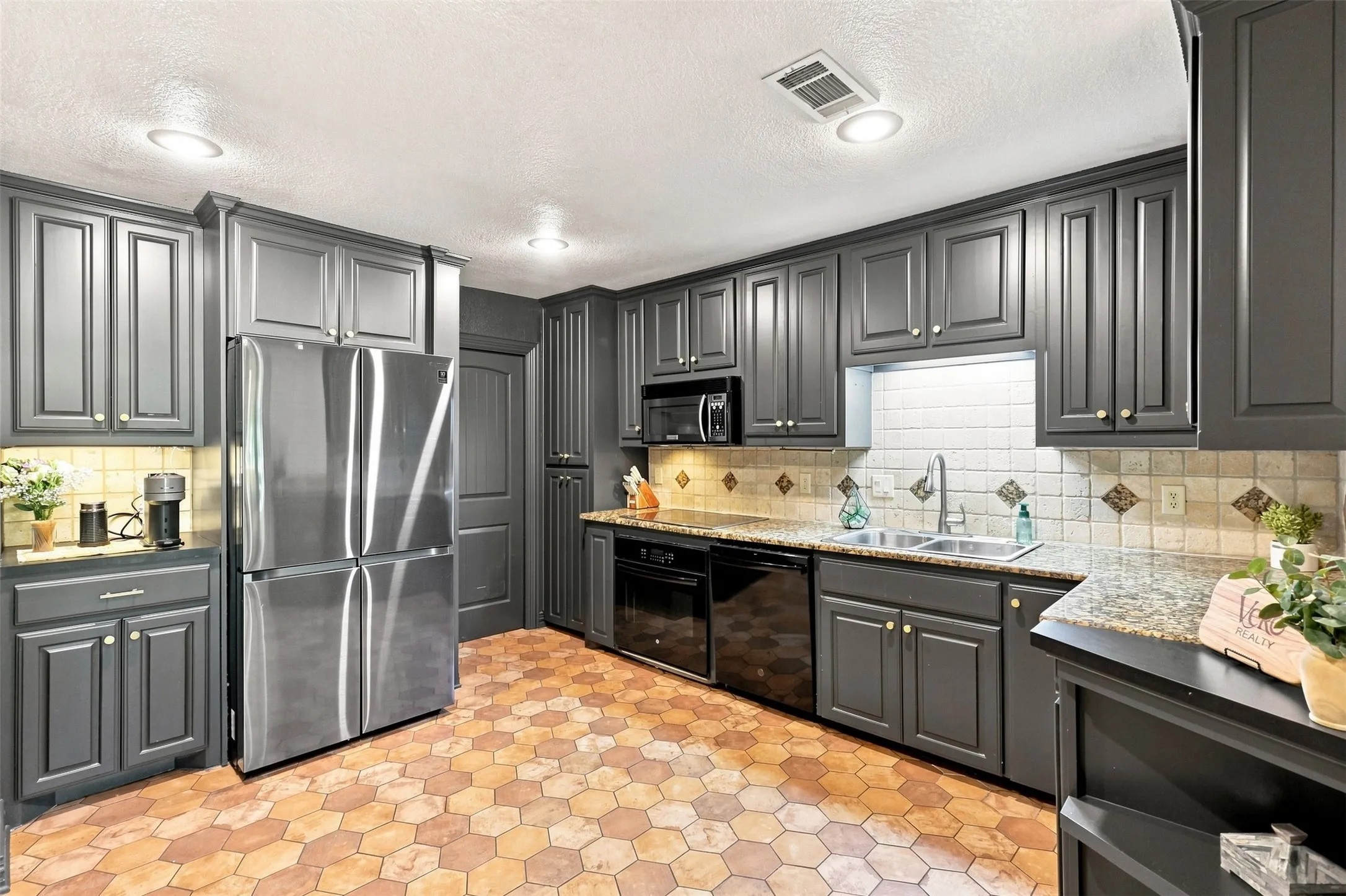 Kitchen featuring dark-toned cabinetry, hexagonal floor tile, recessed lighting, and a stainless steel refrigerator