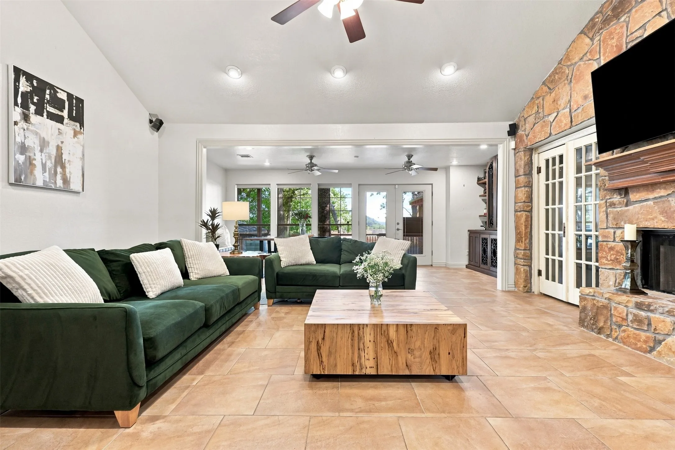 Stone-clad fireplace with a wood mantle, light tile flooring, recessed lighting, and a ceiling fan