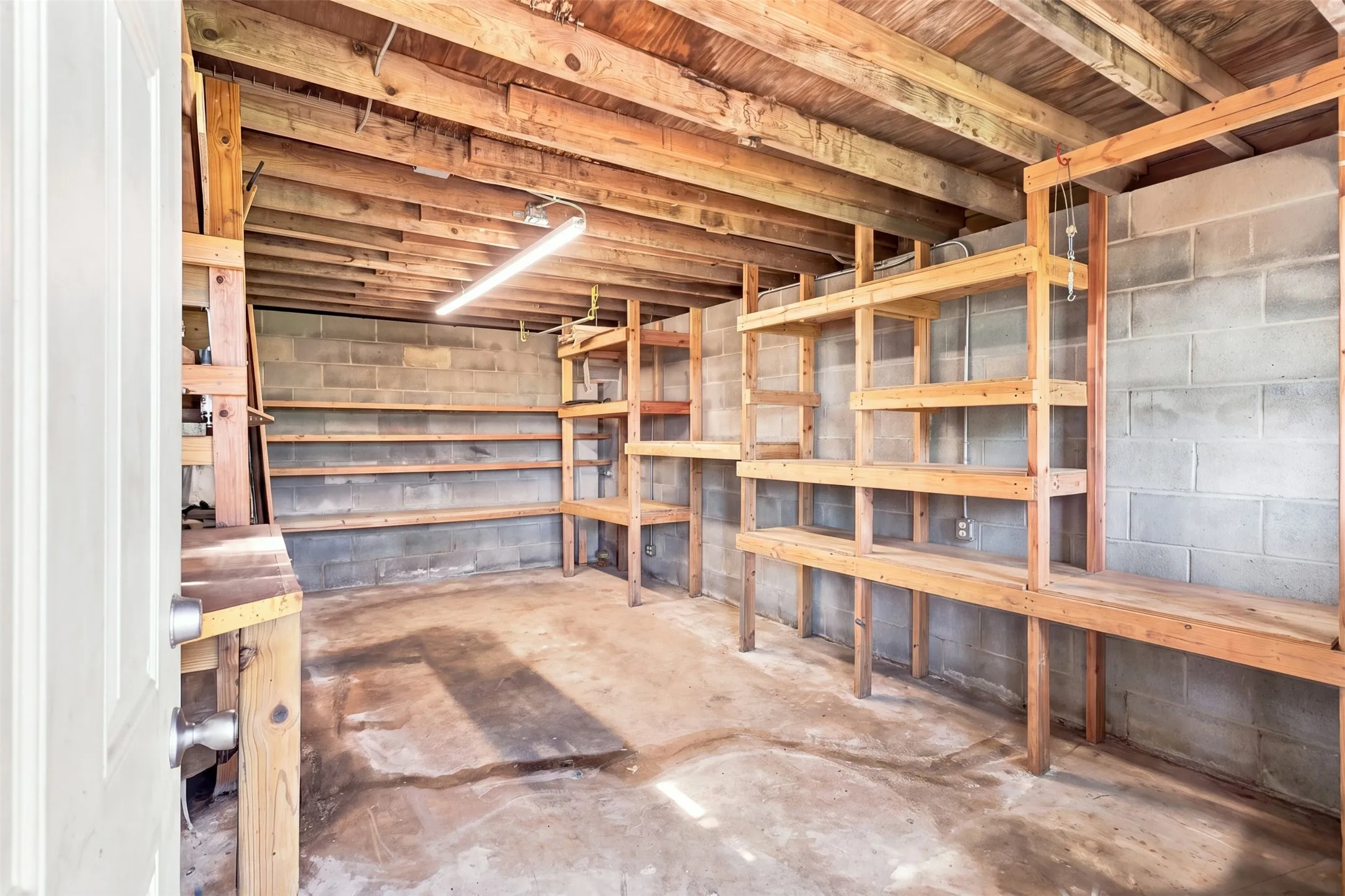 Boat house with electricity    Unfinished room with built-in wooden shelving, exposed wood beam ceiling, concrete block walls, and concrete flooring