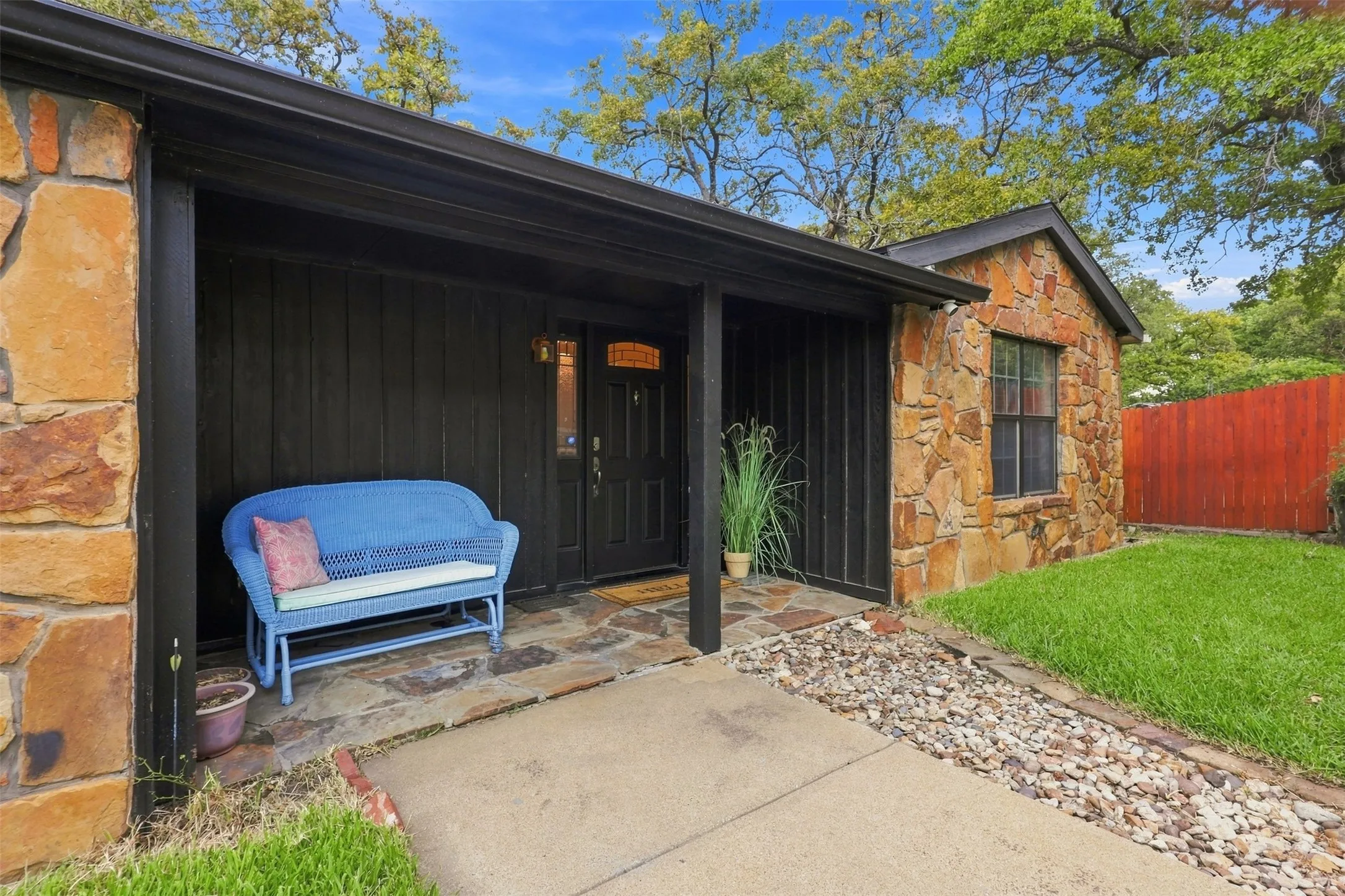 Stone exterior with black siding, covered entryway, flagstone porch, and a wood entry door