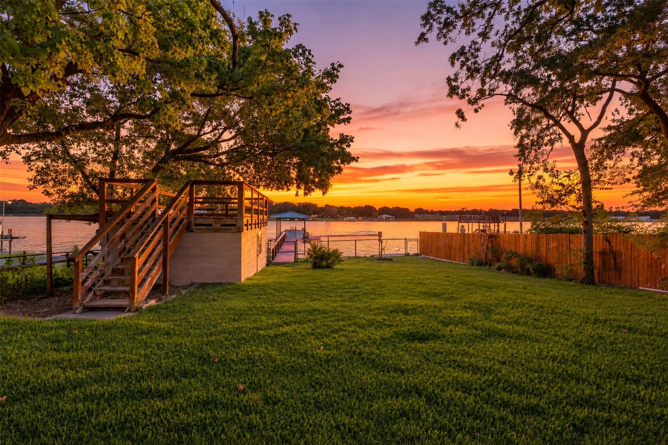 Expansive green lawn, multi-level wooden deck, private wooden dock, waterfront access, and mature trees