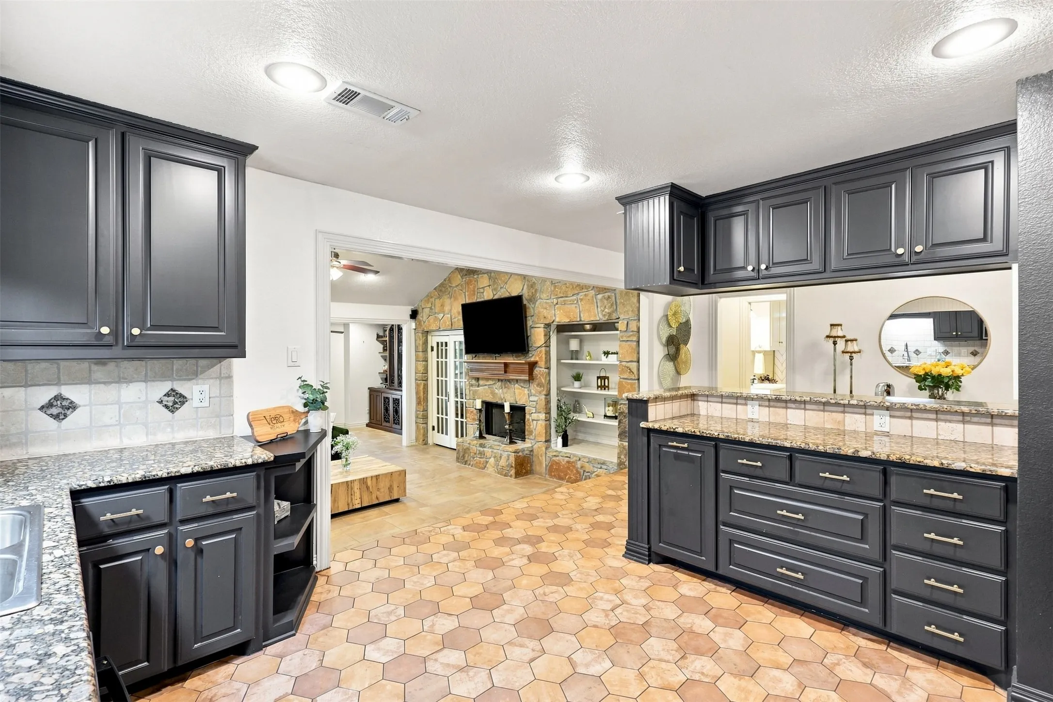 Dark cabinetry, granite-finish countertops, tile backsplash, hexagonal floor tiles, and a pass-through window