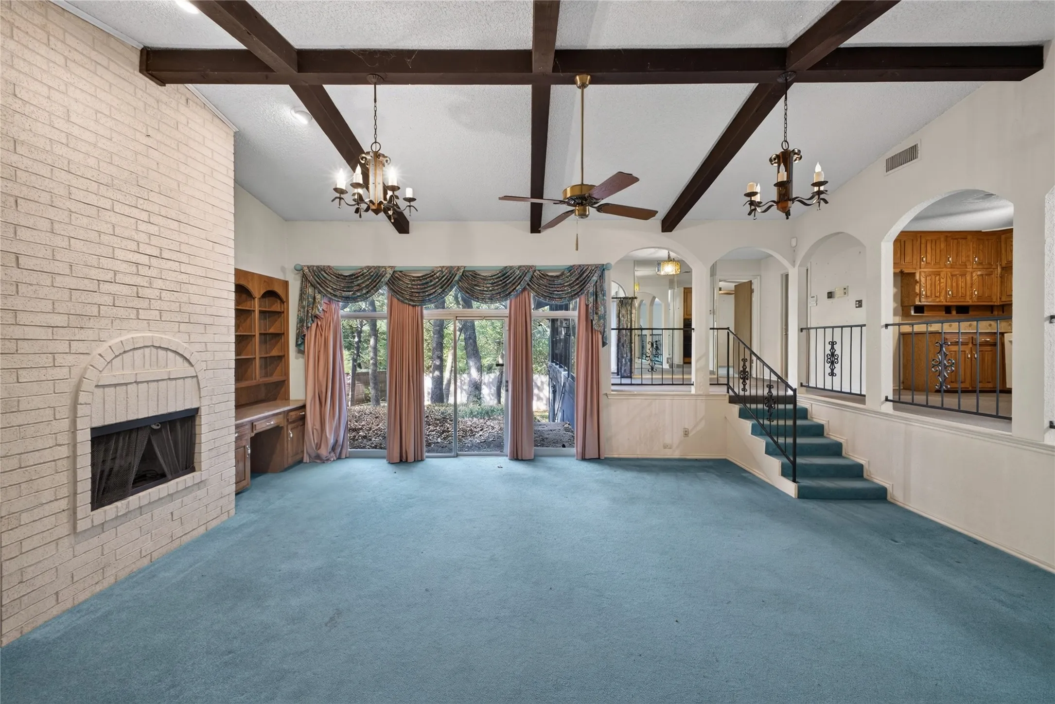 Vaulted family room with exposed wood beams, floor-to-ceiling brick fireplace and wall of glass overlooking the backyard.