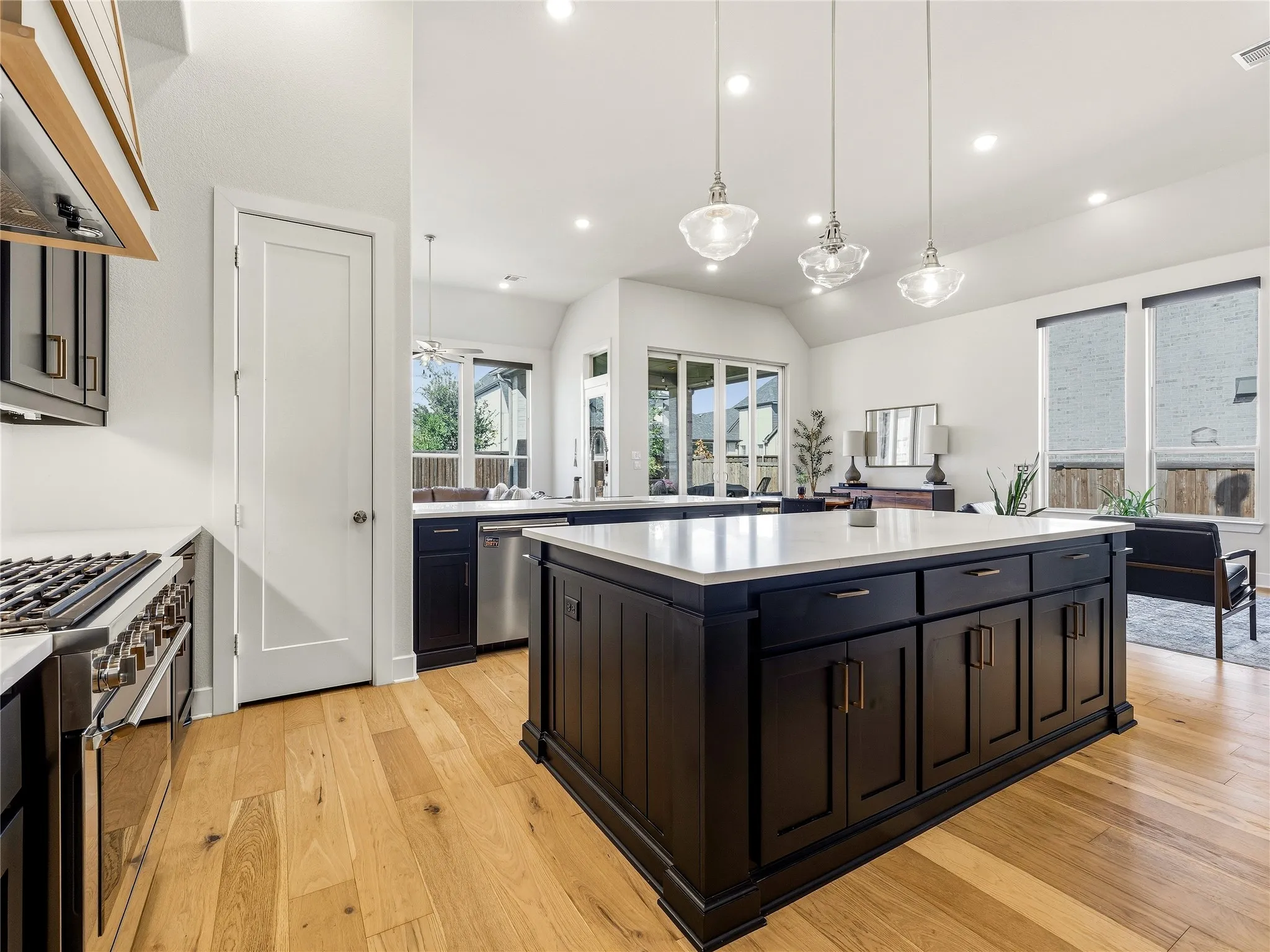Central kitchen island with dark cabinetry and light-toned countertop, wood-finish flooring, stainless steel range, and recessed lighting
