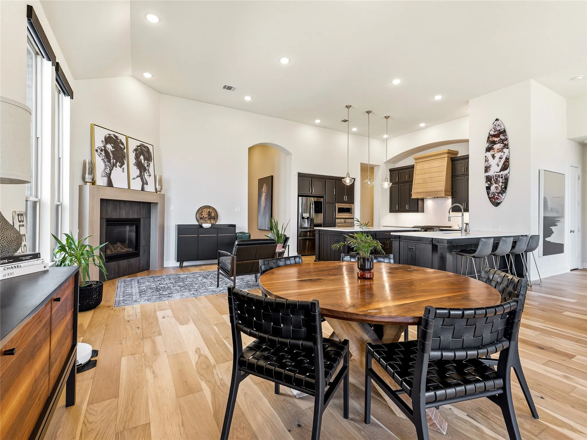 Vaulted ceilings, a built-in fireplace with a hearth, wood-finish flooring, a kitchen island with seating, and pendant lighting fixtures