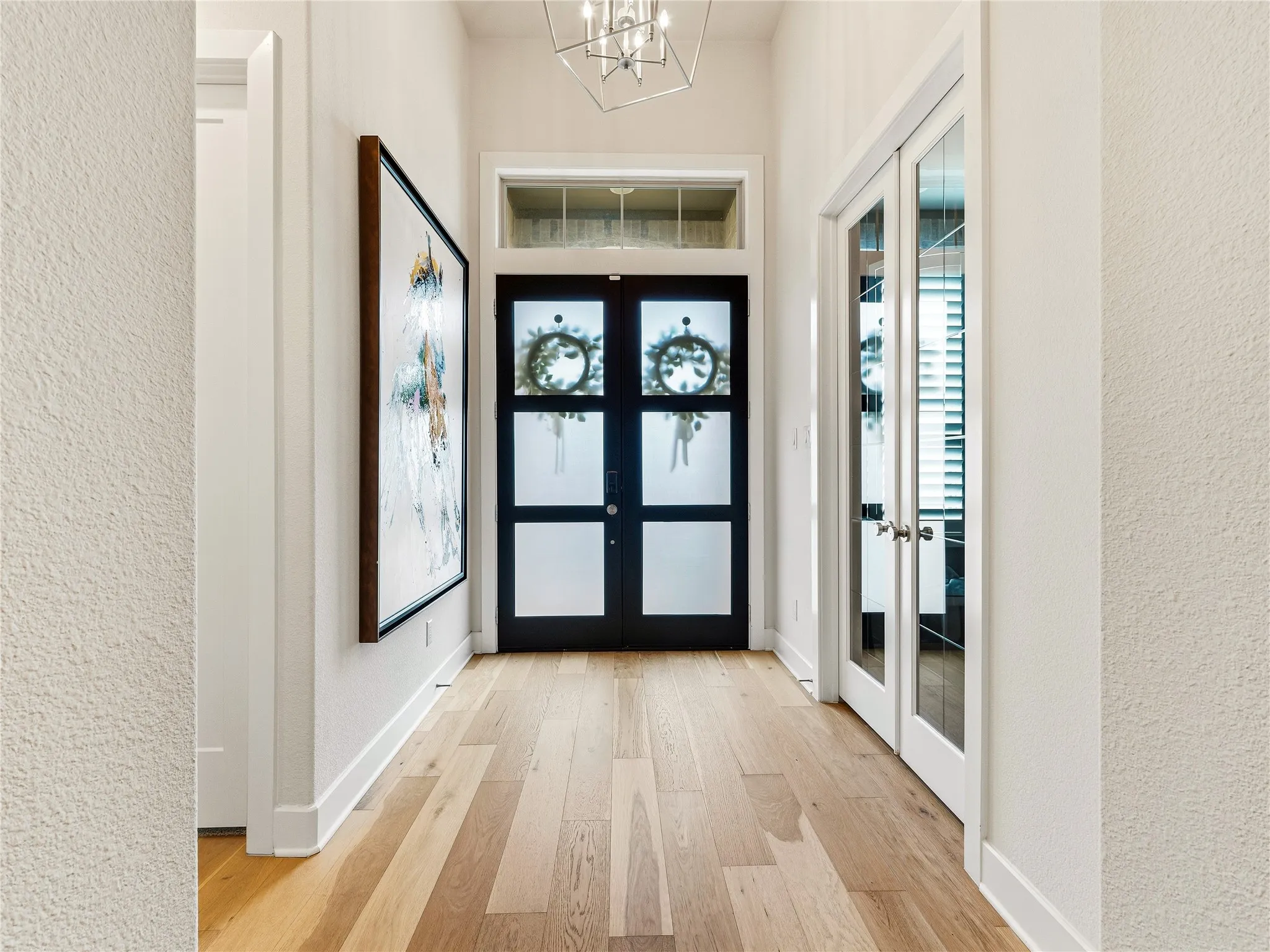 Hardwood-finish flooring, a contemporary chandelier, a transom window, a black paneled entry door, and double French doors