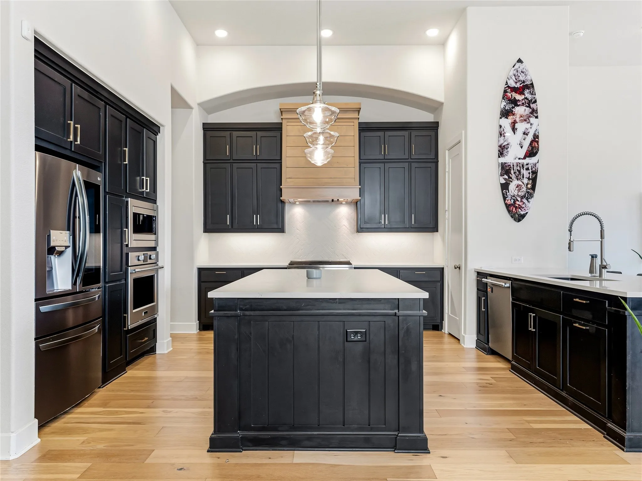 Kitchen featuring dark cabinetry, stainless steel appliances, a center island with a light-colored countertop, wood-finish flooring, and recessed lighting