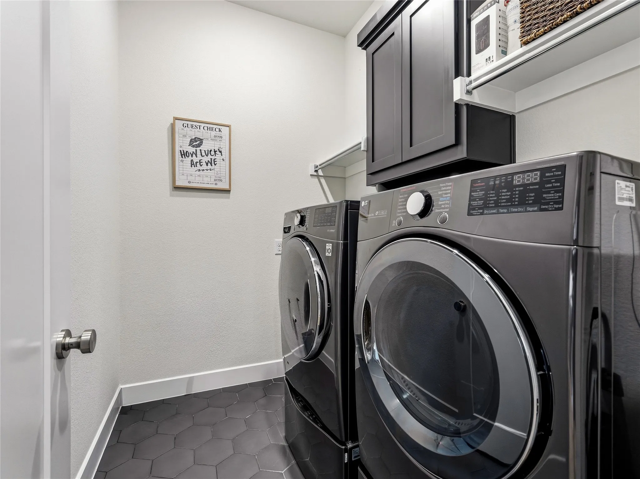 Laundry area featuring dark hexagon floor tiles, white walls, built-in shelving, and dark cabinetry