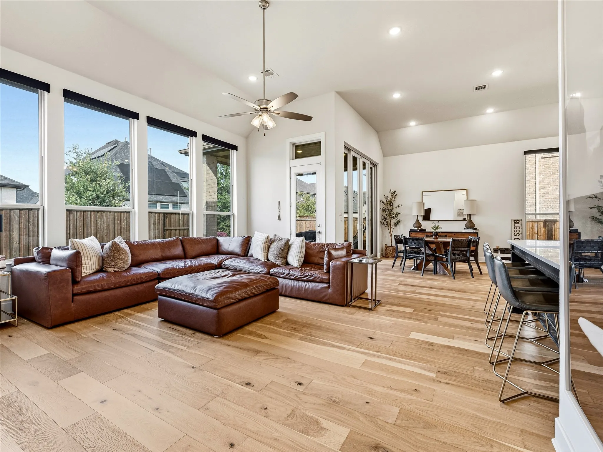 Vaulted ceiling with recessed lighting and a ceiling fan, wood-finish flooring, full-height windows, and sliding glass doors