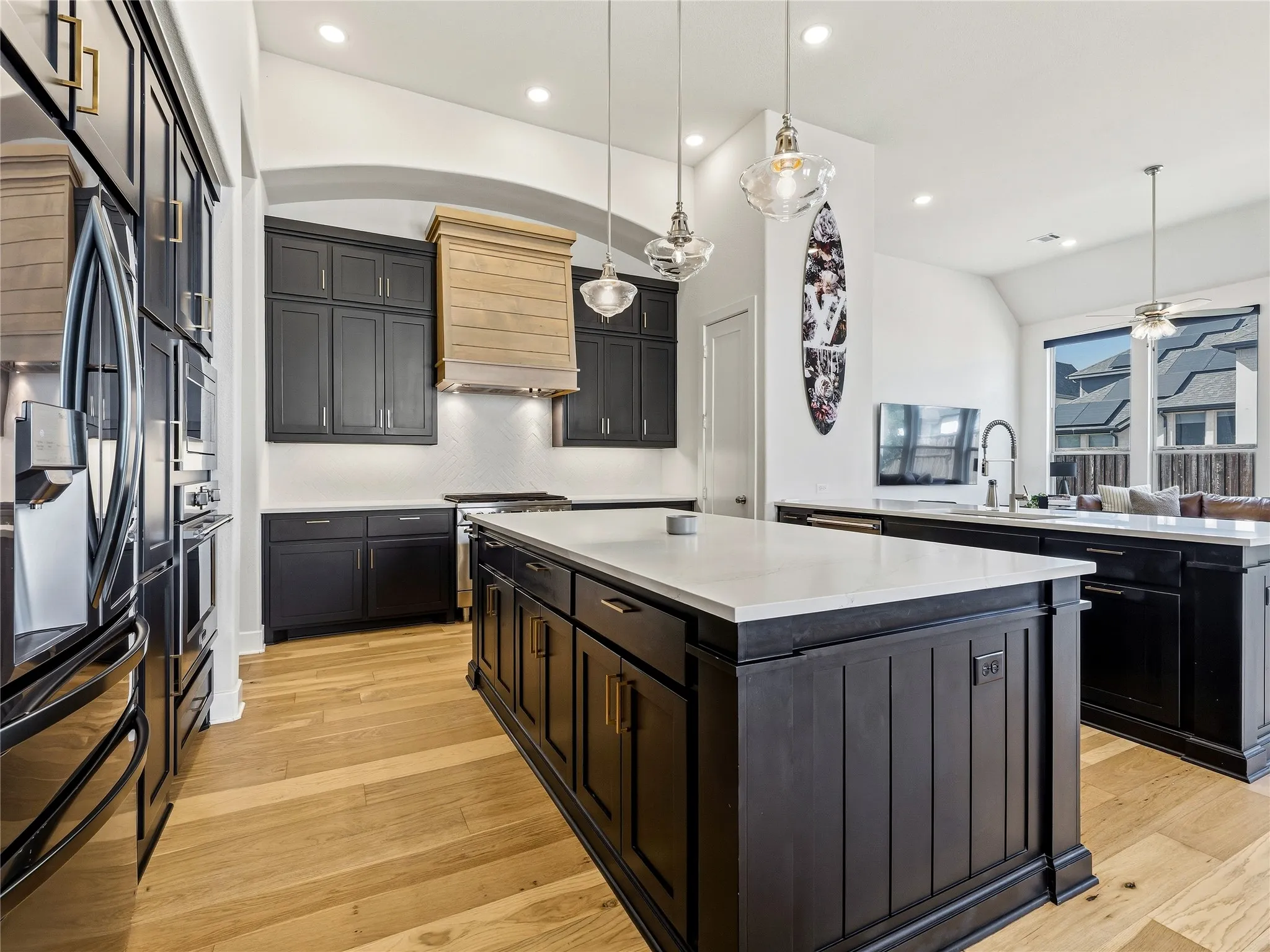 Expansive kitchen featuring wood-finish flooring, dark cabinetry, a large kitchen island with a light-toned countertop, a built-in range hood, and recessed lighting