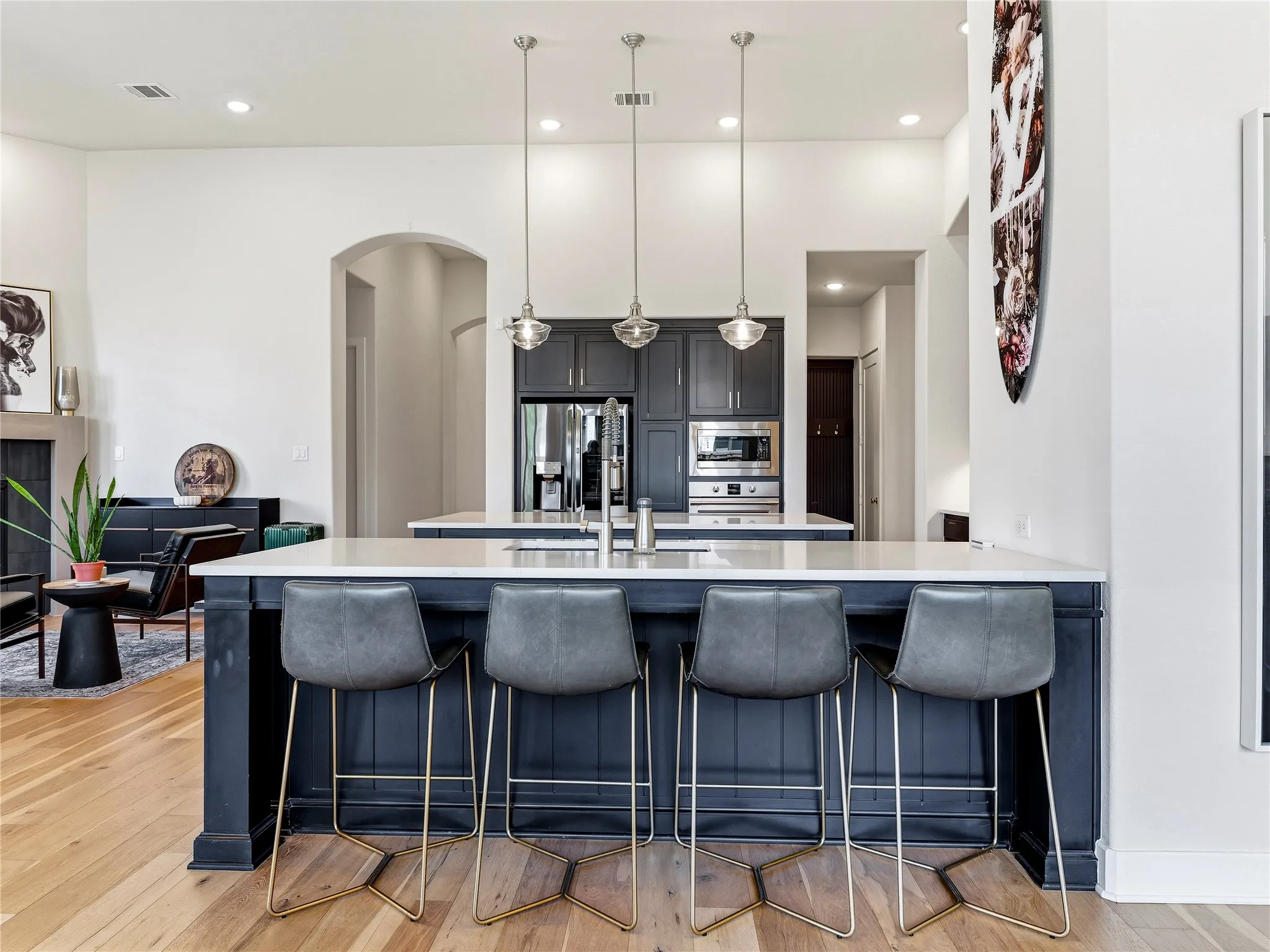 Kitchen island with a light-colored countertop, pendant lighting, stainless steel appliances, dark cabinetry, and wood-finish flooring