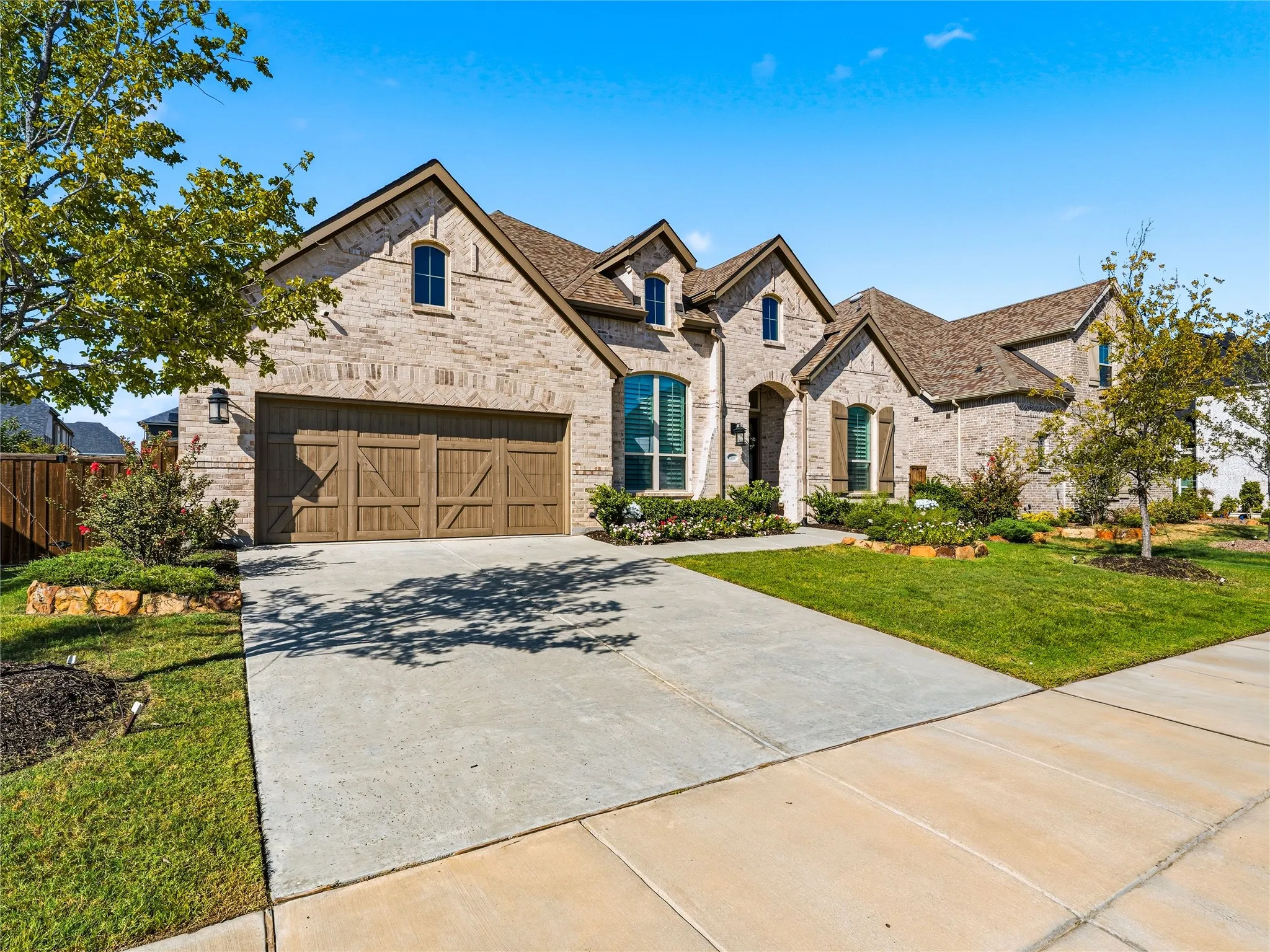 Brick facade with stone accents, arched windows, decorative wooden garage doors, concrete driveway, and front landscaping