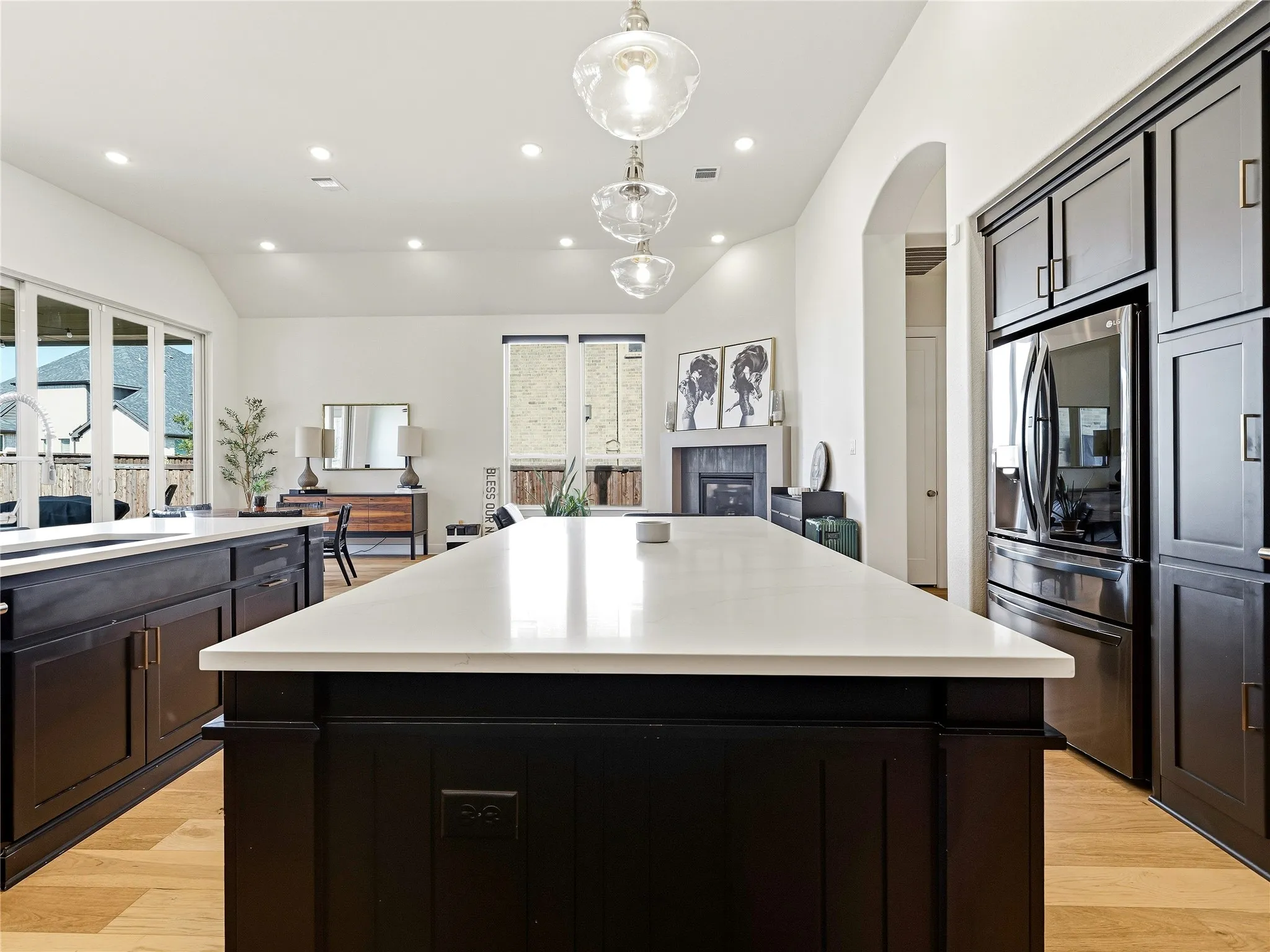 Spacious kitchen featuring an expansive central island, dark cabinetry, stainless steel appliances, and a vaulted ceiling with recessed lighting