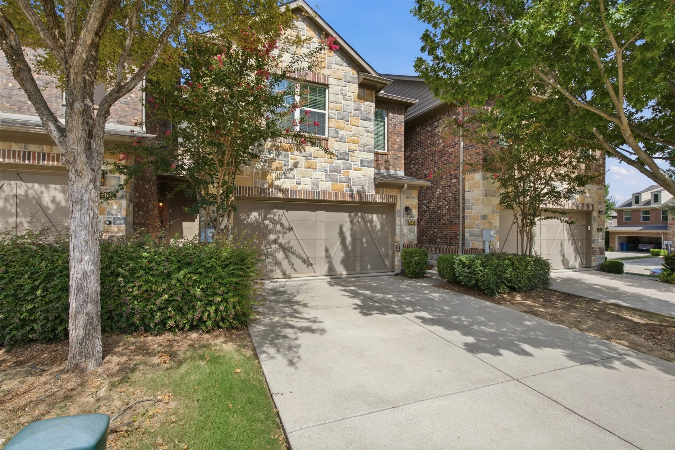 Stone and brick exterior with multiple garage bays, concrete driveways, and mature landscaping