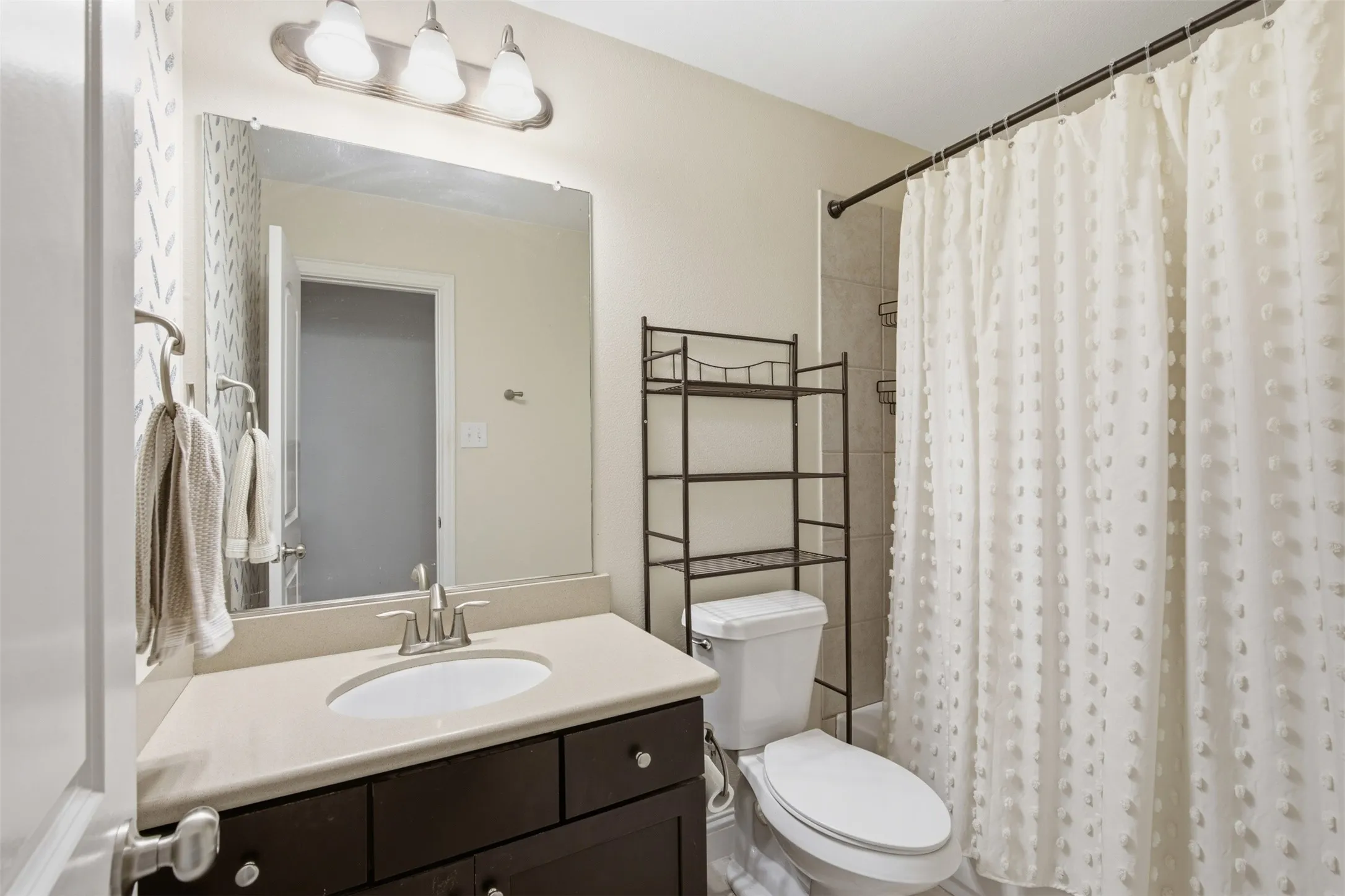 Bathroom featuring a single vanity with an undermount sink, a large mirror, and a three-light fixture