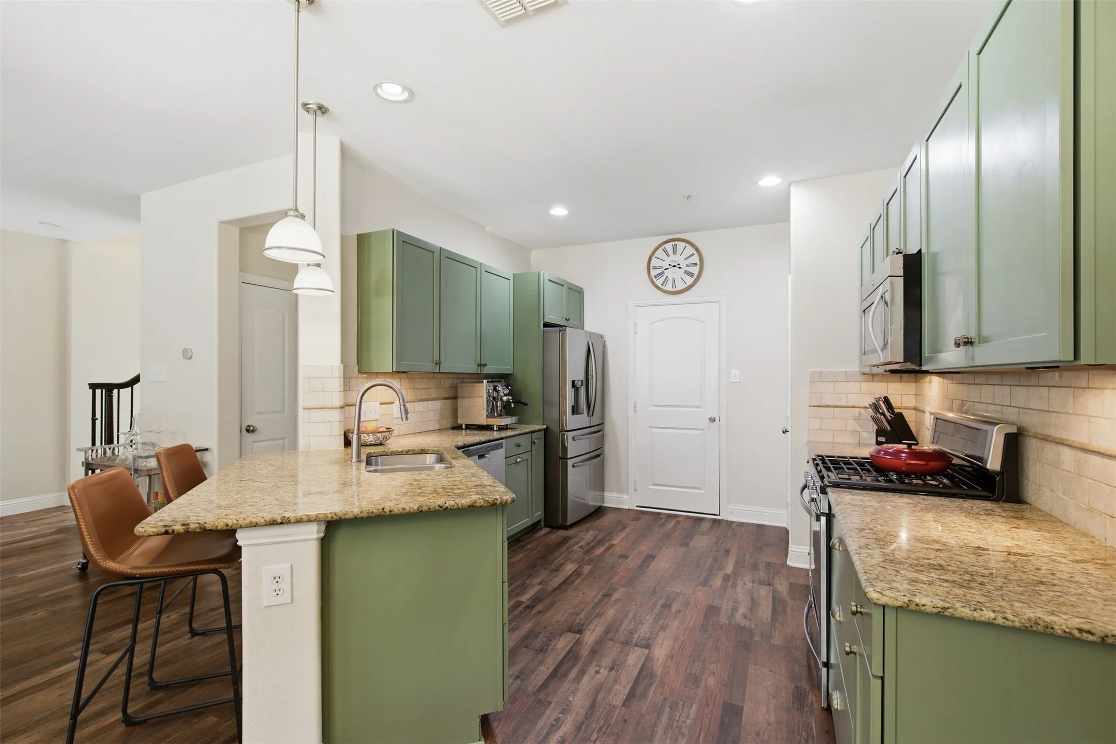 Kitchen featuring green cabinetry, granite countertops, stainless steel appliances, wood-finish flooring, and a subway tile backsplash
