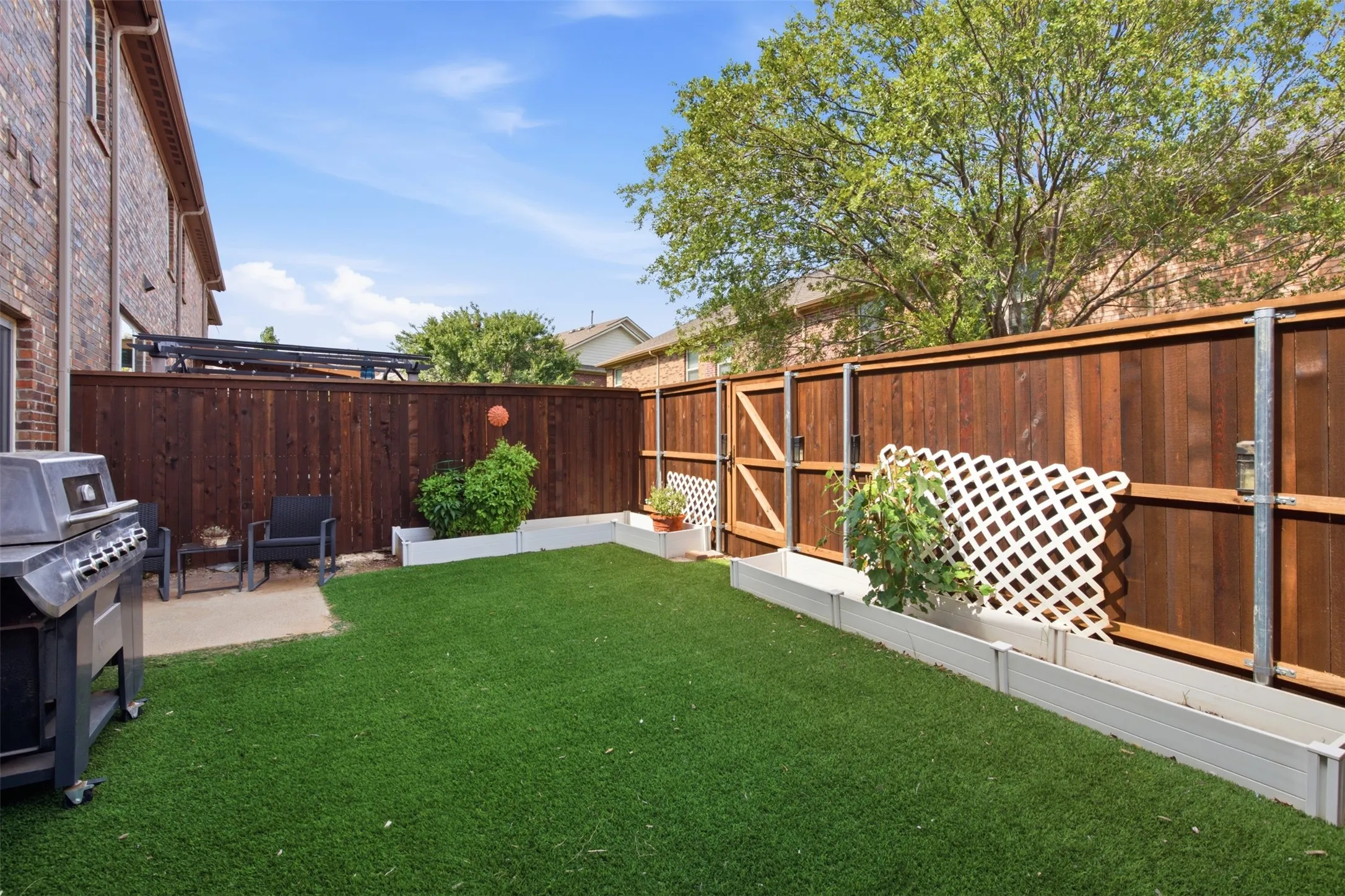 Private backyard featuring artificial turf, a wood privacy fence, and raised garden beds