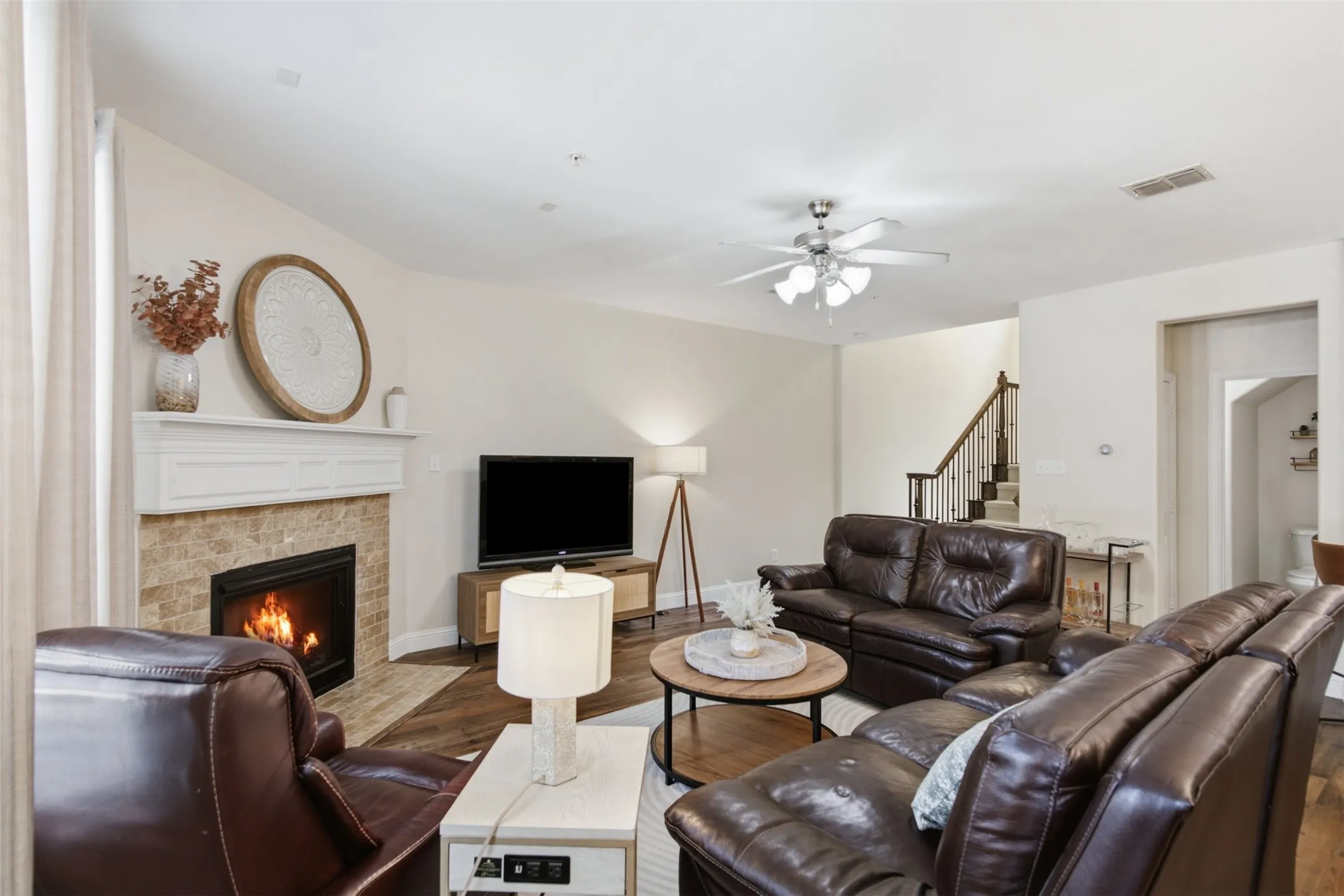 Living area featuring a fireplace with a stone surround and white mantel, wood-finish flooring, and a ceiling fan