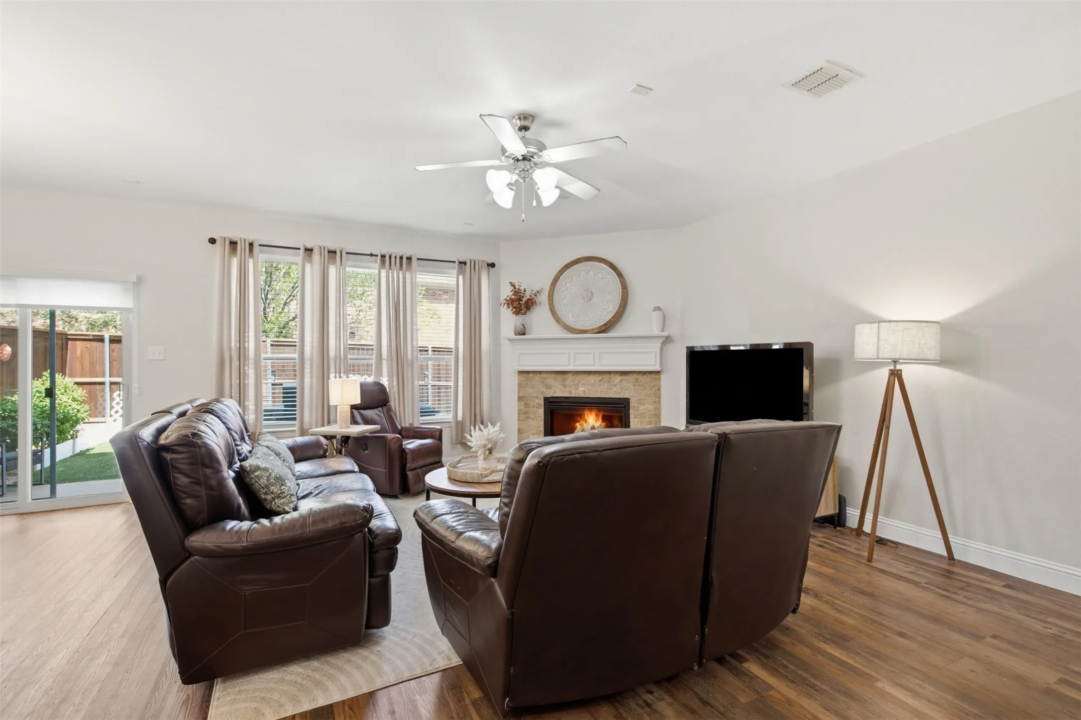 Living area featuring wood-finish flooring, a white mantel fireplace with stone surround, a ceiling fan, and a sliding glass door to the exterior