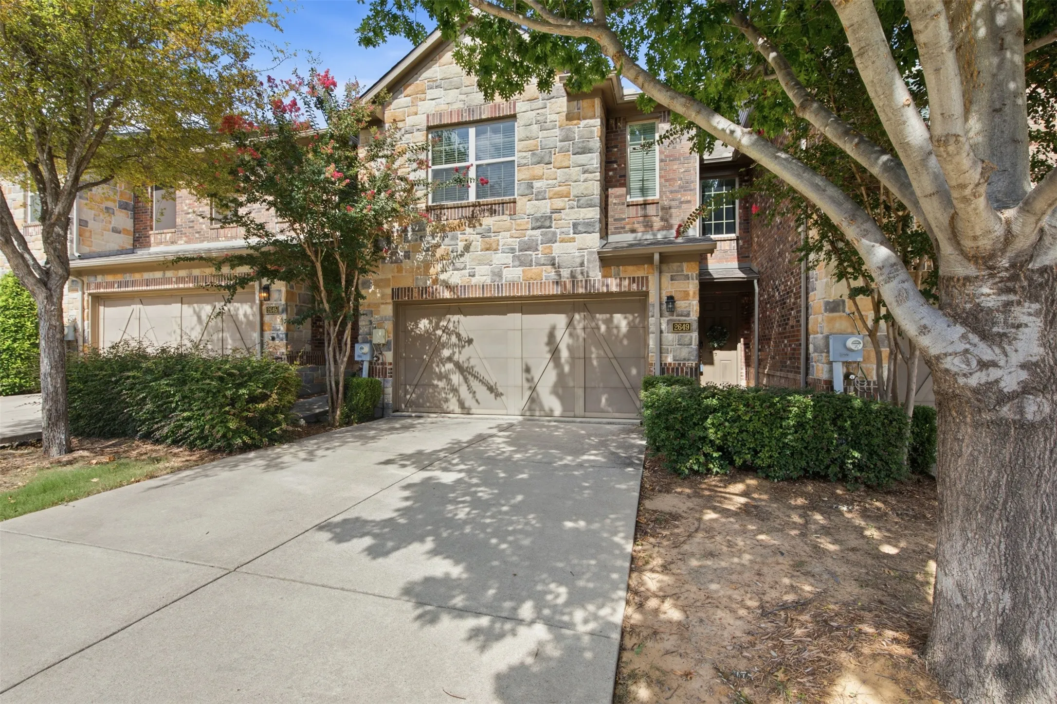 Stone and brick facade, two-car garage, mature landscaping, concrete driveway, and covered entry