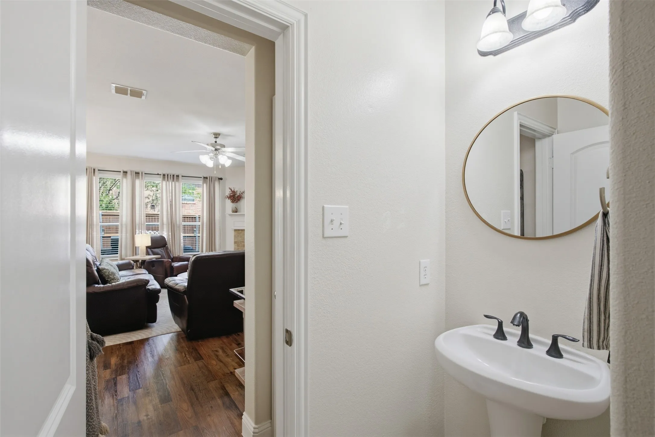 Pedestal sink with dark-finish faucet, oval mirror, and wall-mounted vanity lighting