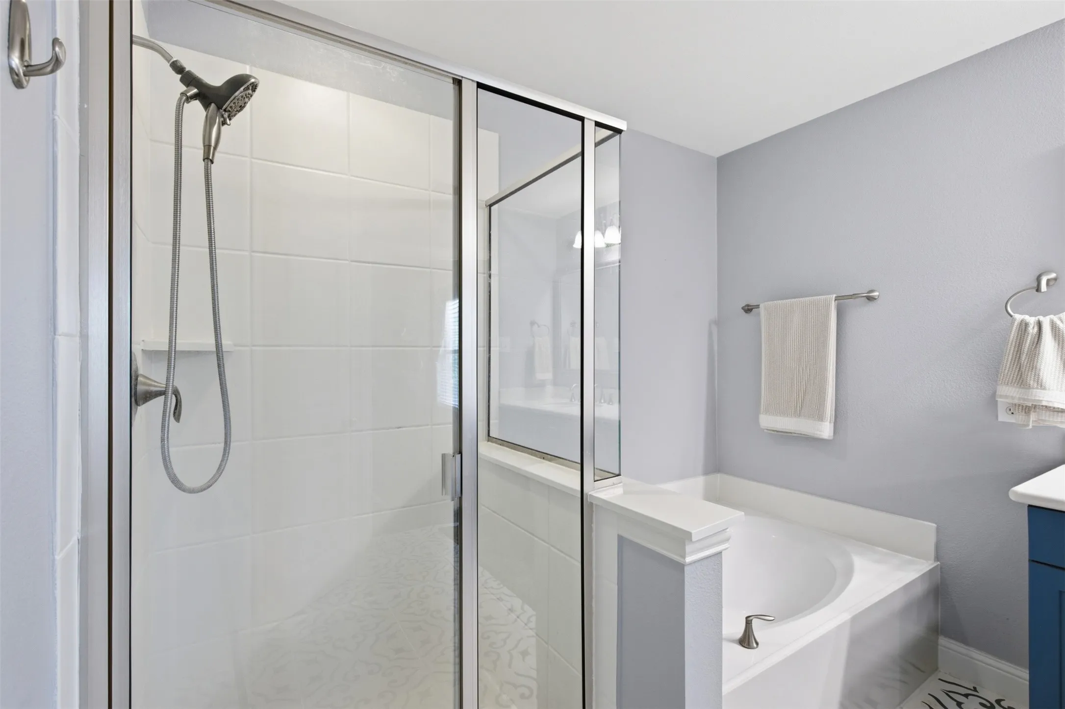 Glass-enclosed shower with white subway tile surround, separate built-in soaking tub, brushed nickel shower fixtures, and light gray wall paint