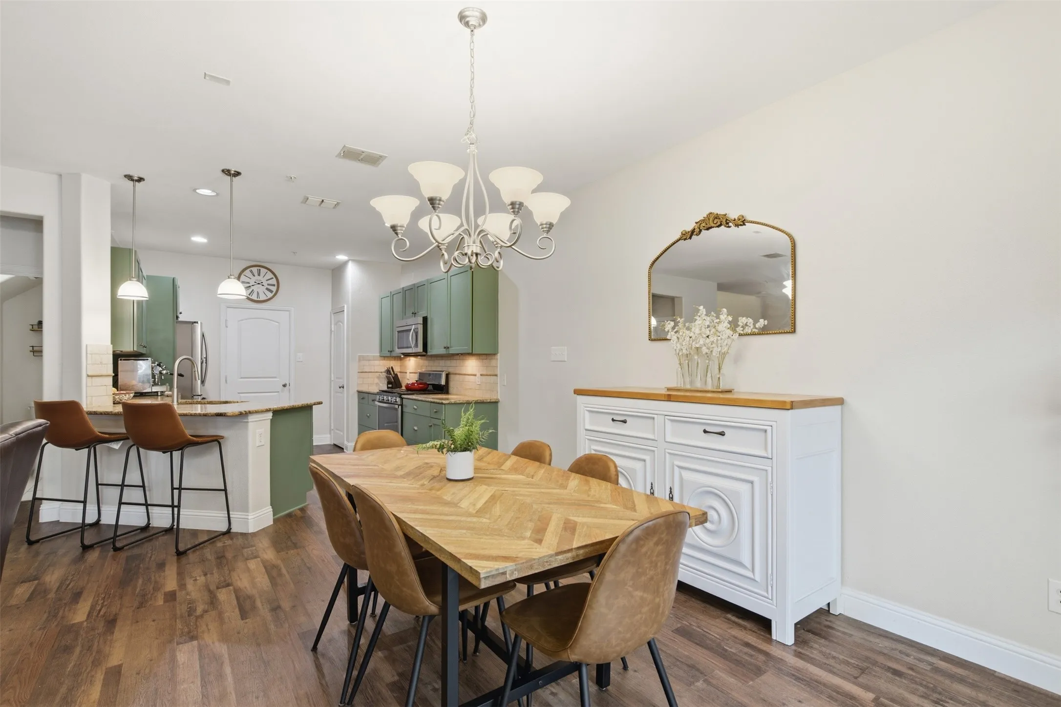 Open-concept living space with wood-finish flooring, a kitchen featuring green cabinetry, stainless steel appliances, and a breakfast bar