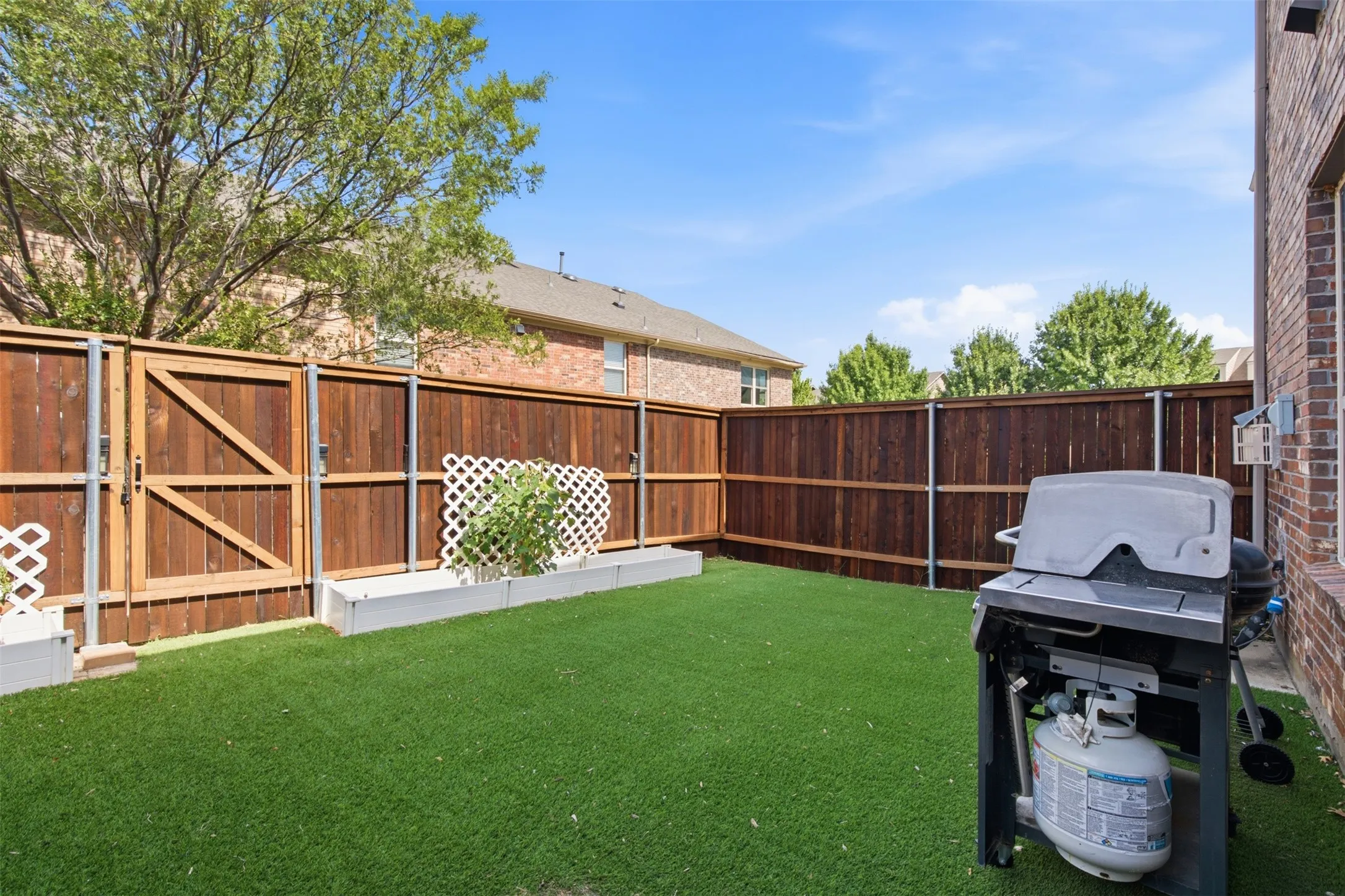 Enclosed backyard featuring artificial turf, a wood privacy fence, and a gate