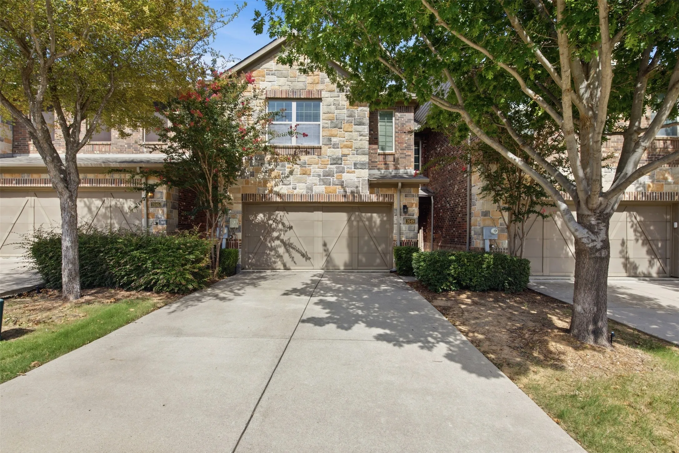 Stone and brick exterior with a two-car garage and mature trees