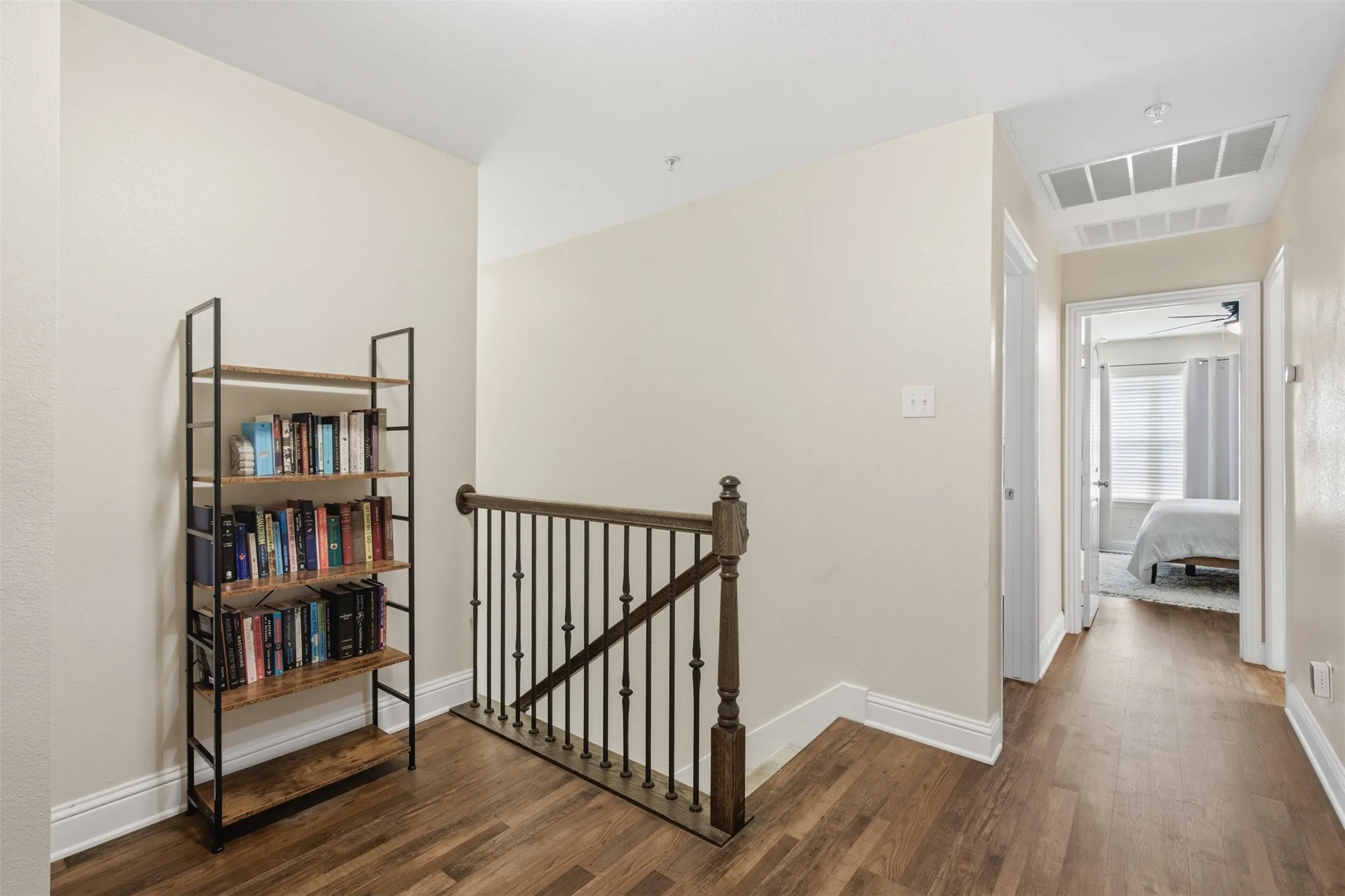 Wood-finish flooring throughout the hallway, featuring a built-in staircase railing with dark wood and metal spindles