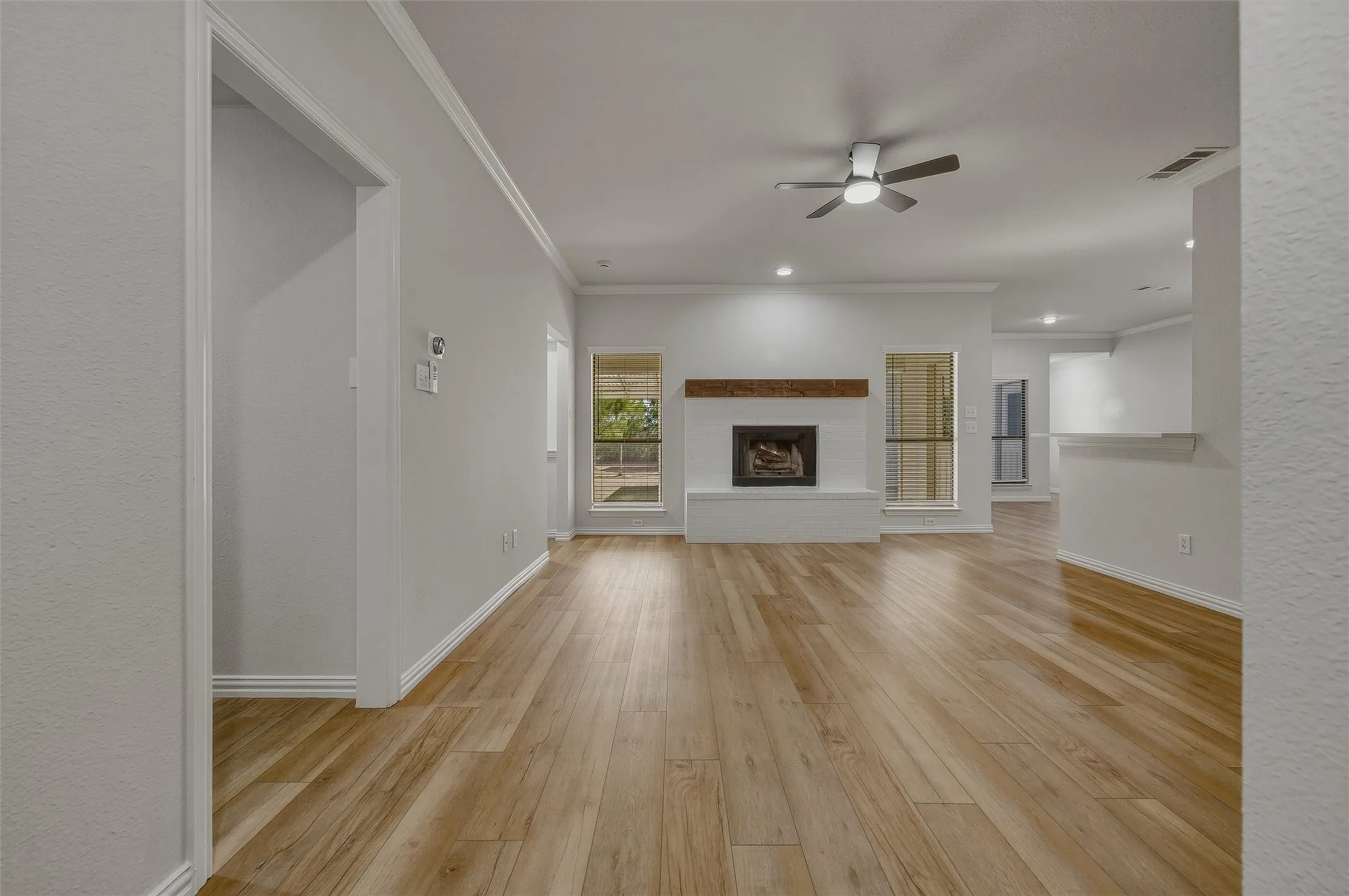 Wood-finish flooring throughout, white painted brick fireplace with a wood mantel, crown molding, recessed lighting, and a ceiling fan