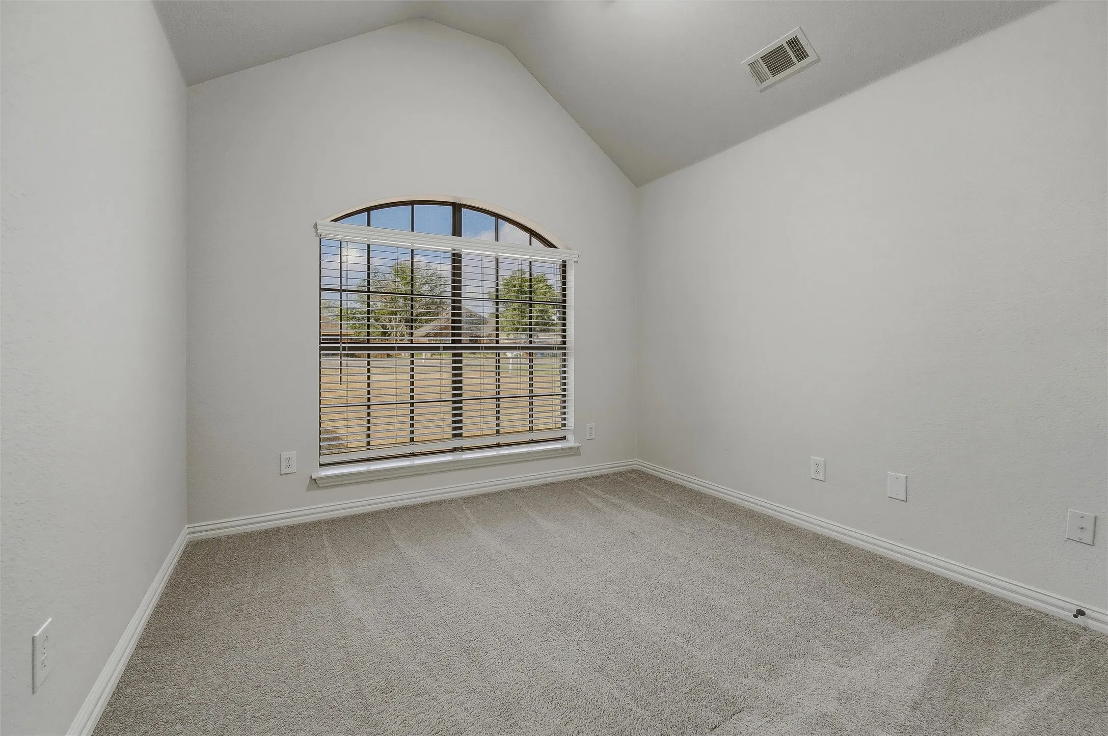 Arched window with blinds, vaulted ceiling, neutral wall paint, and gray carpet