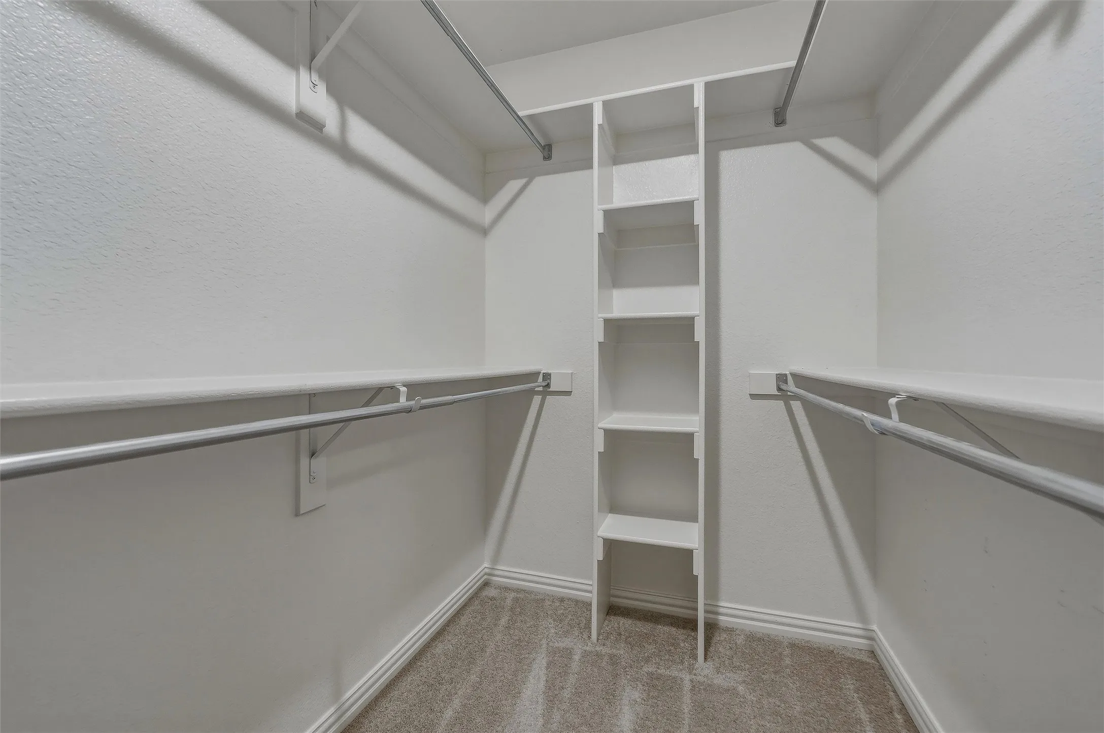 Walk-in closet featuring carpeted flooring, white shelving, and hanging rods