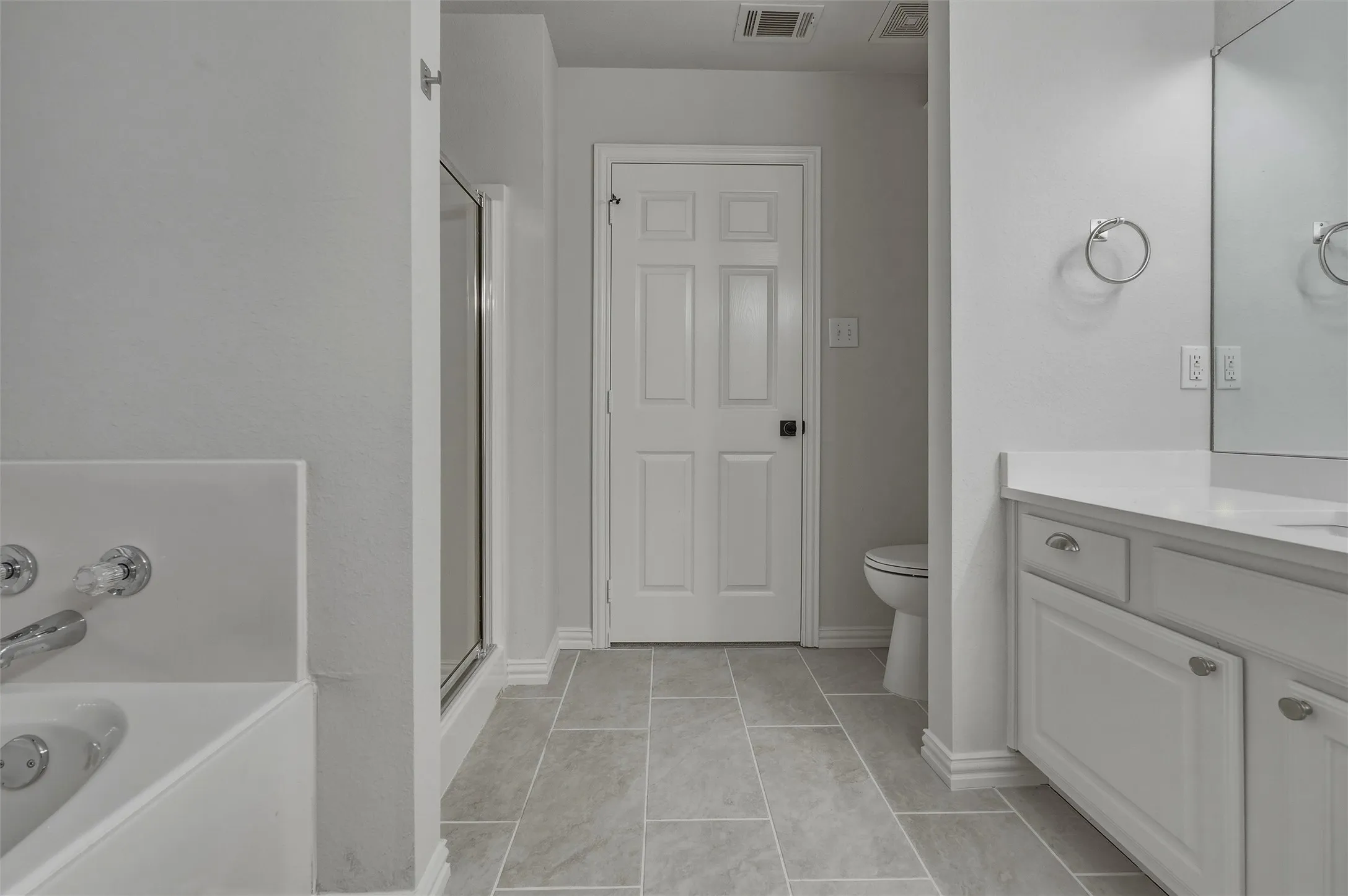 Bathroom featuring light tile flooring, a built-in tub with chrome fixtures, a glass-enclosed shower, a vanity with a white countertop and double sinks, and a commode