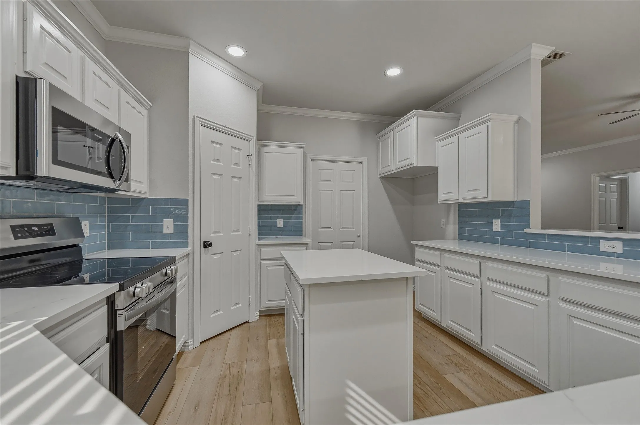 Kitchen featuring white shaker-style cabinetry, stainless steel appliances, a light-toned wood-finish floor, white countertops, and a blue subway tile backsplash