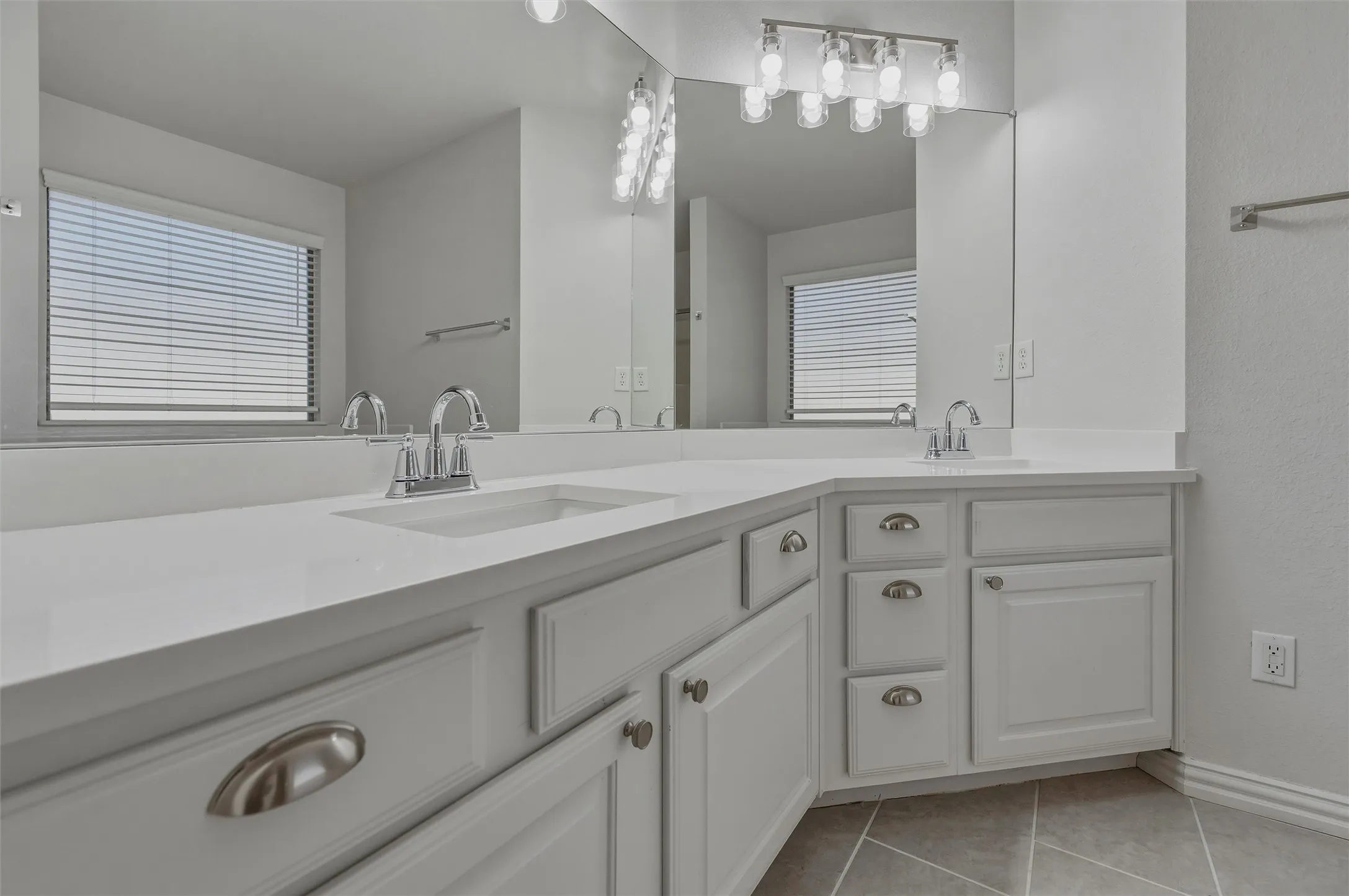 Dual vanity with white cabinetry, integrated sinks, chrome fixtures, and overhead bar lighting