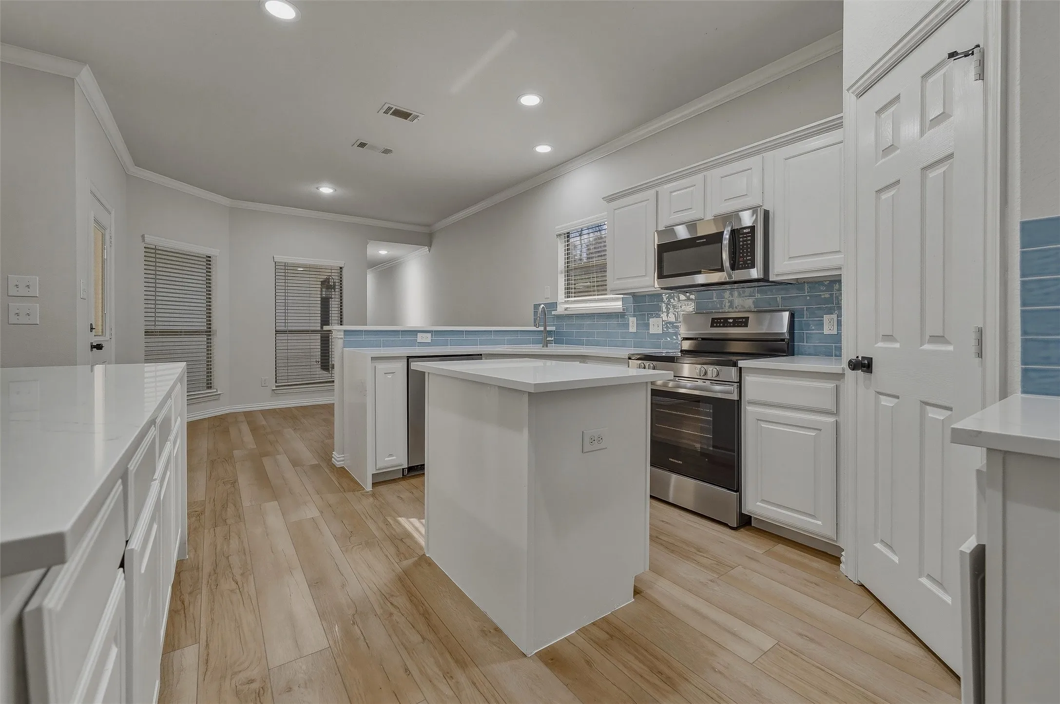 Kitchen featuring white cabinetry, light-toned wood-finish flooring, stainless steel appliances, blue tile backsplash, and recessed lighting