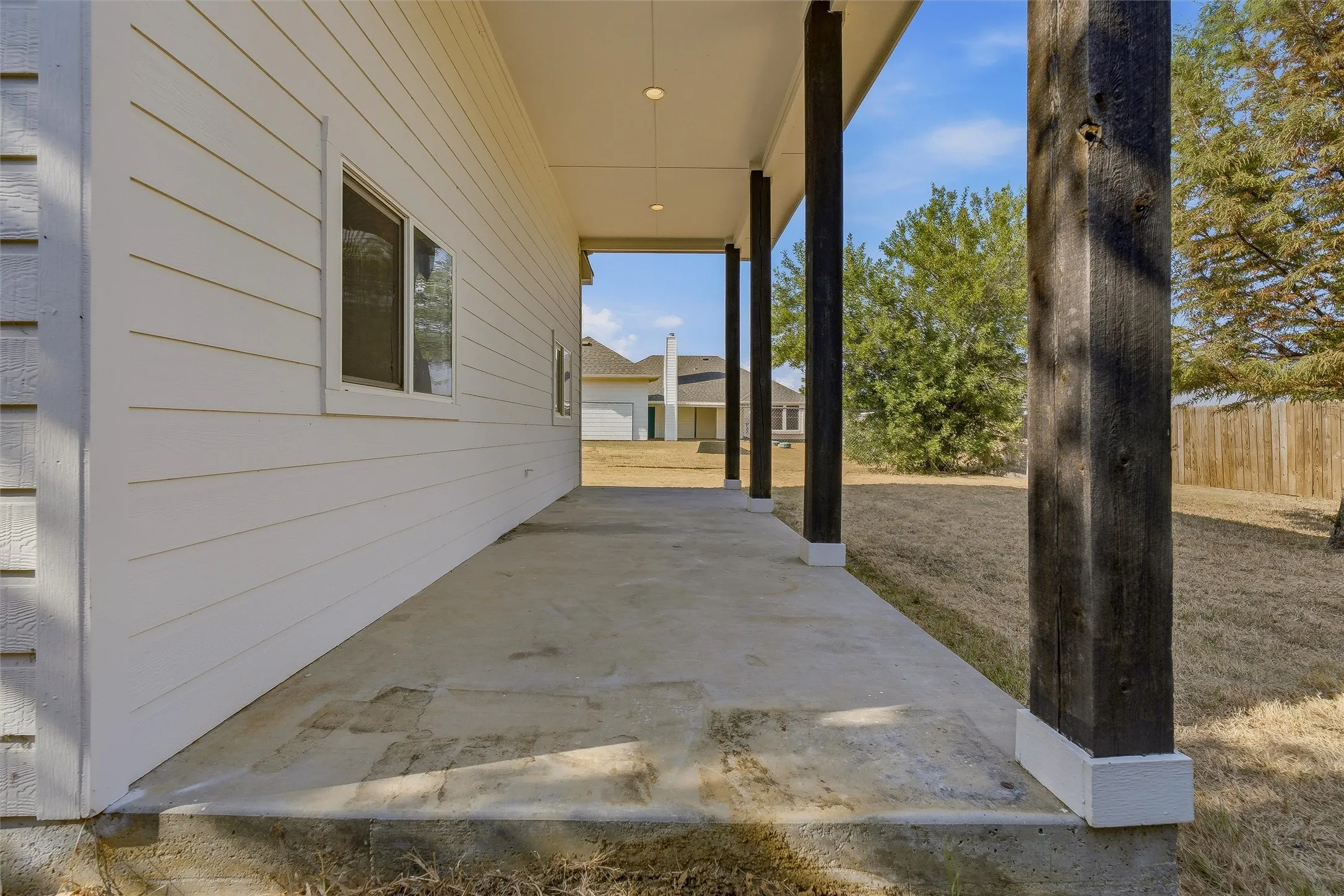 Concrete patio with dark wood-finish support columns and white siding