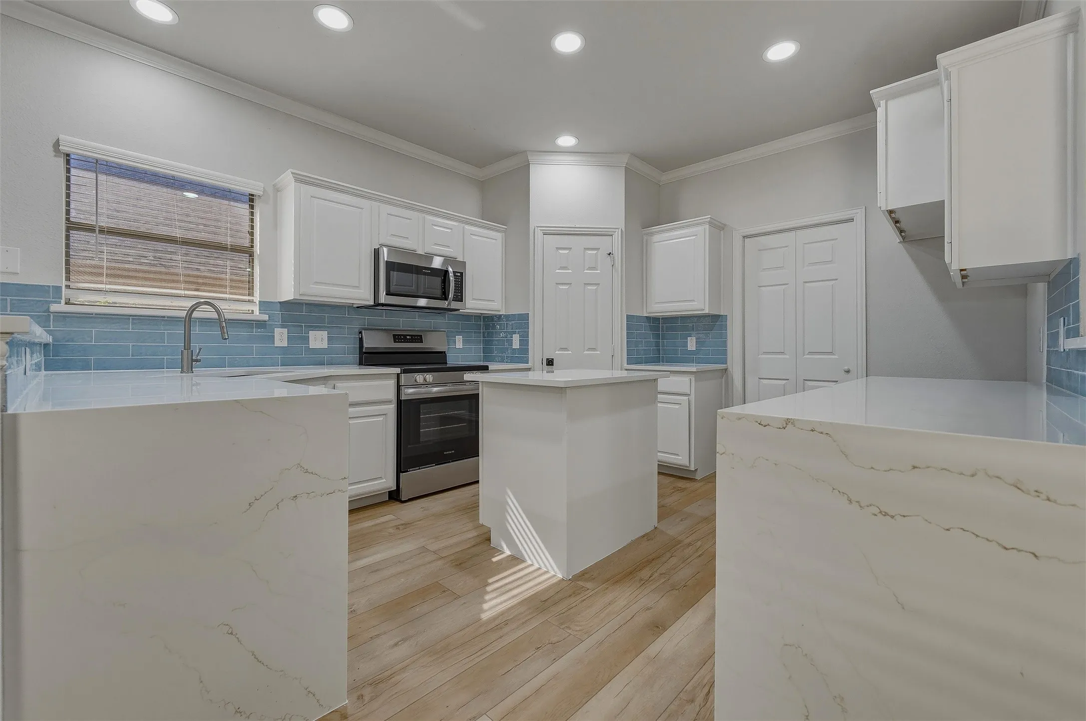 Kitchen featuring white cabinetry, stainless steel appliances, a center island, wood-finish flooring, and a blue tile backsplash