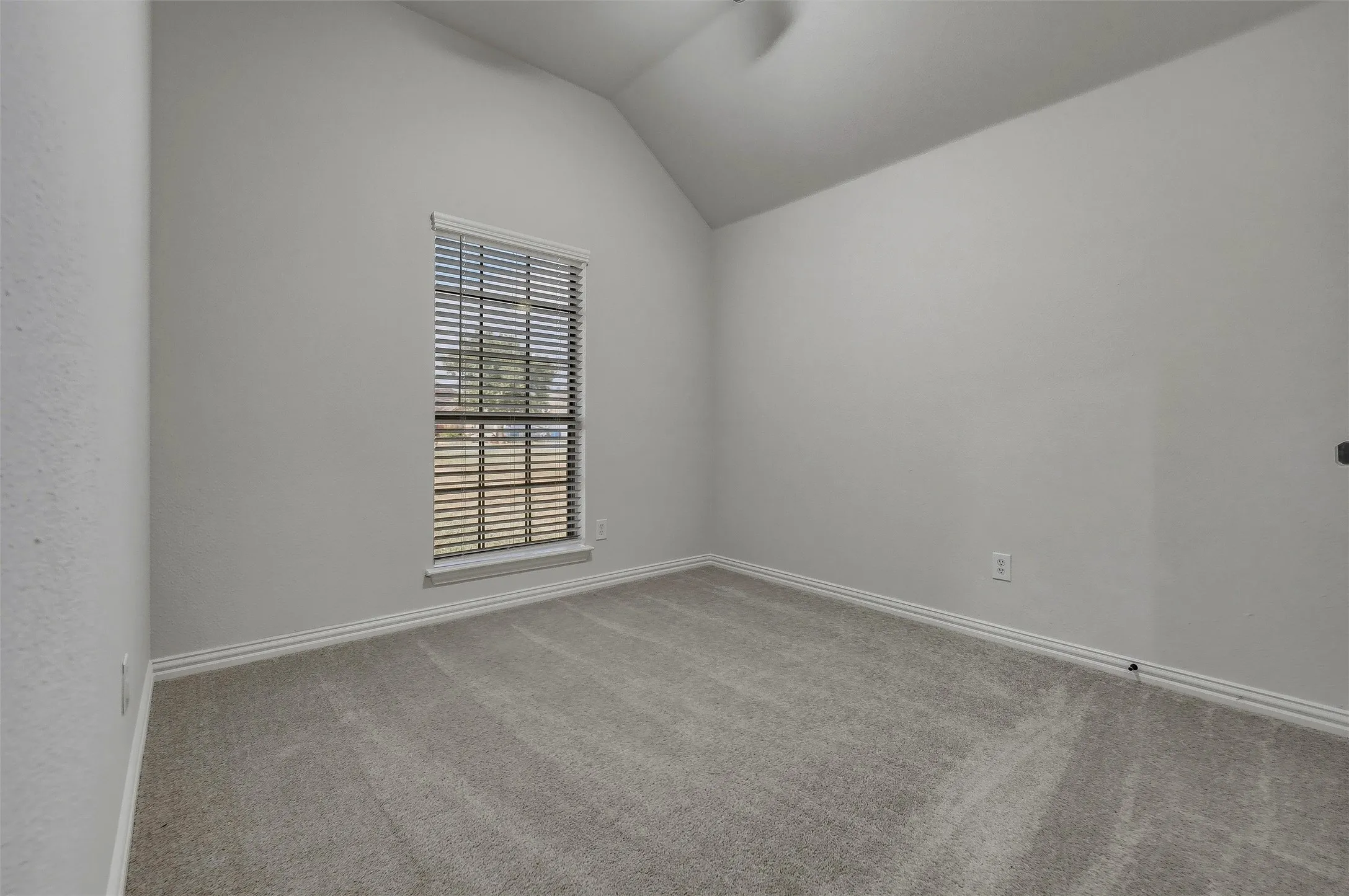 Vaulted ceiling, window with horizontal blinds, neutral wall paint, light-colored carpeting, and a ceiling fan
