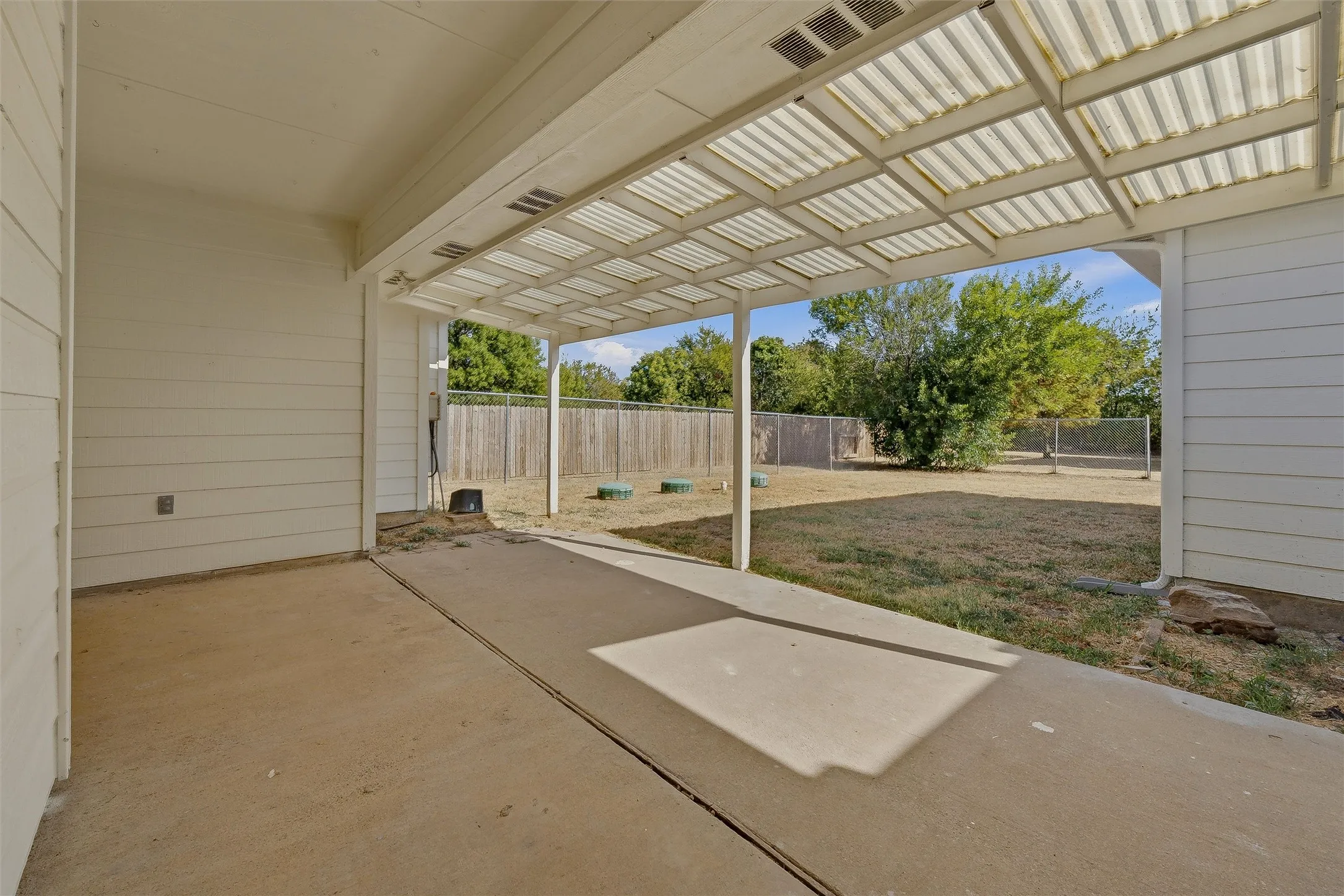 Covered patio with a translucent corrugated roof, concrete flooring, and a fenced backyard